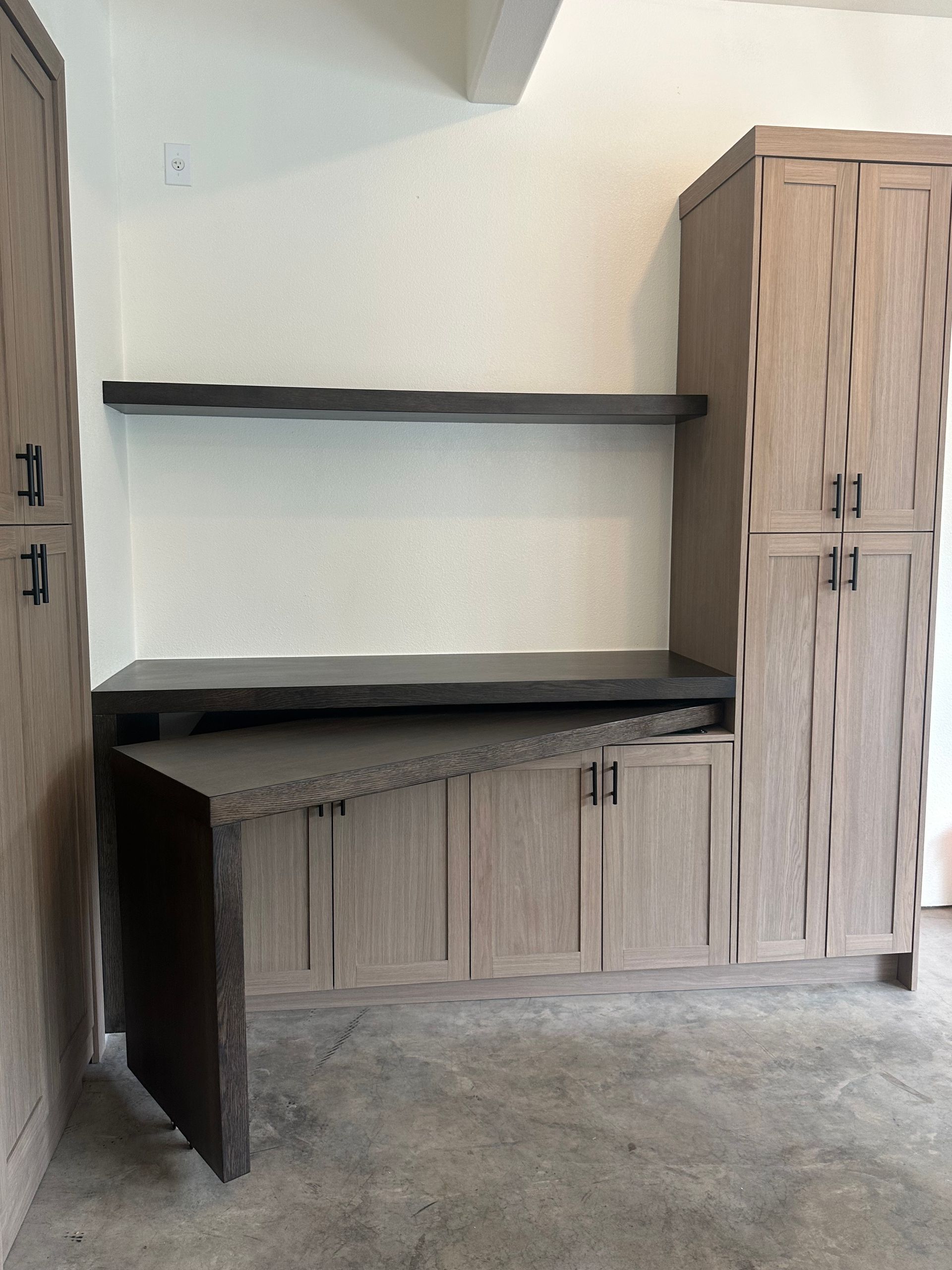 Built-in wooden desk and cabinetry in a room with a light wall and gray floor.