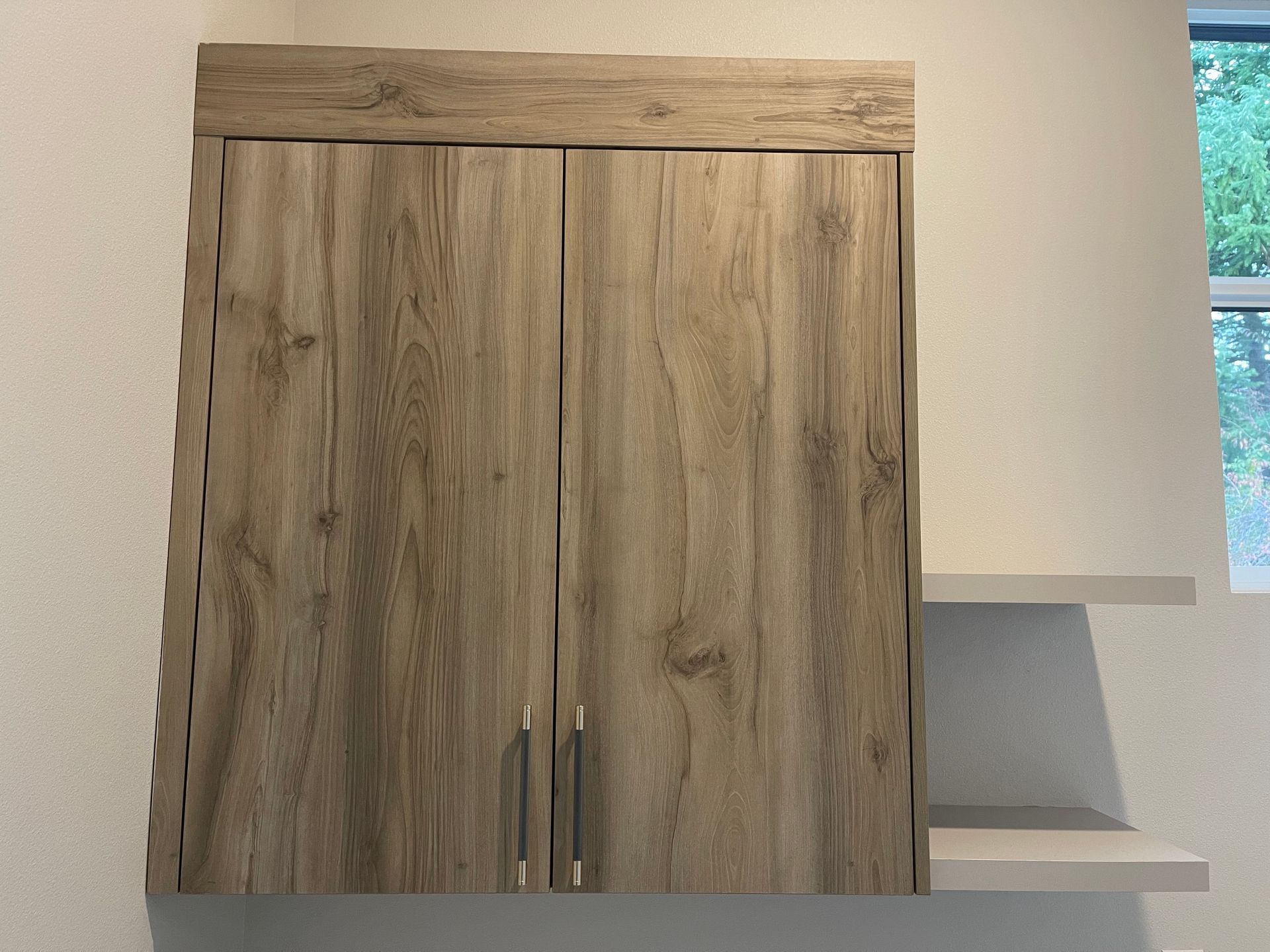 Wooden cabinet with two doors and a shelf, mounted on a white wall.