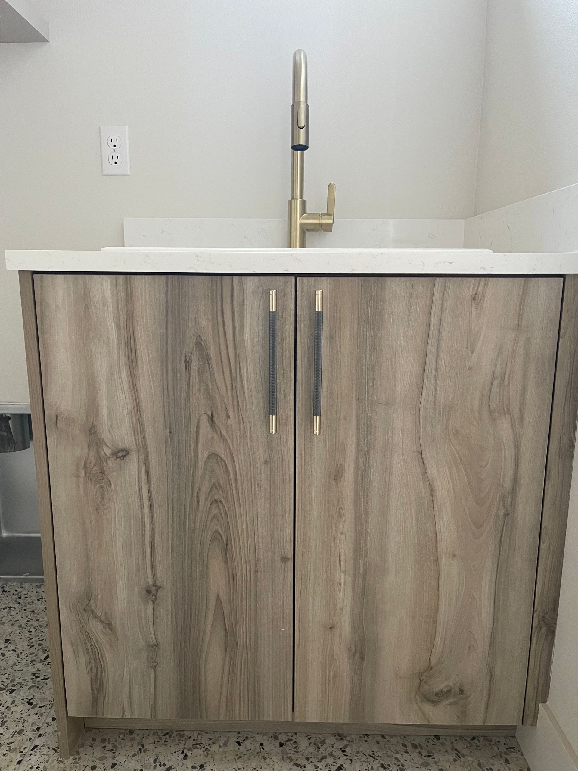 Wooden cabinet with gold faucet and white countertop in room.