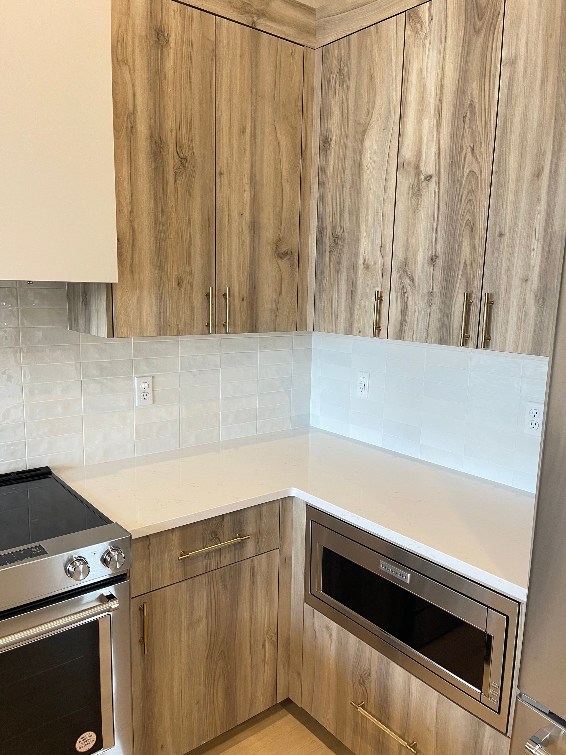L-shaped kitchen with light wood grain cabinets, white countertops, and a built-in microwave and oven.