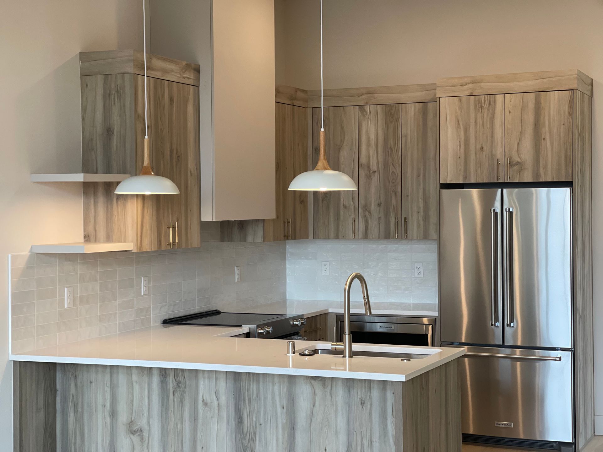 Kitchen with light wood cabinets, stainless steel appliances, white countertops, and pendant lights.