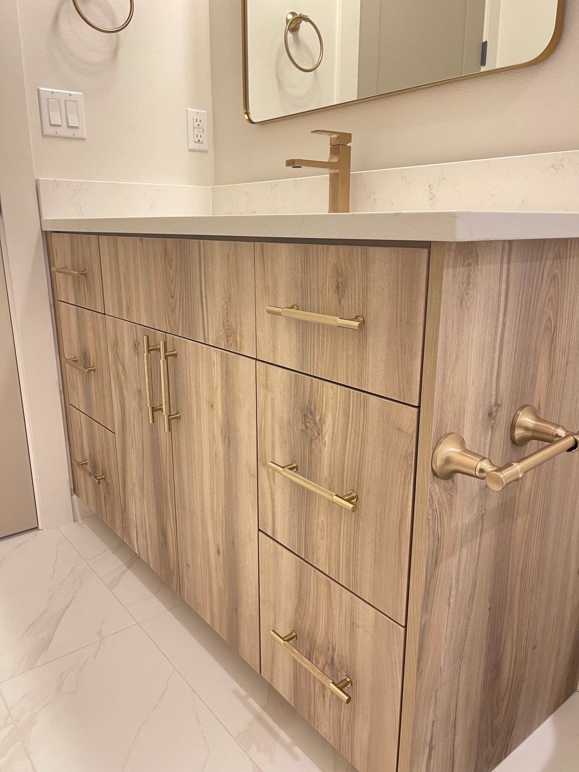 Wooden bathroom vanity with gold hardware, white countertop, and gold faucet.