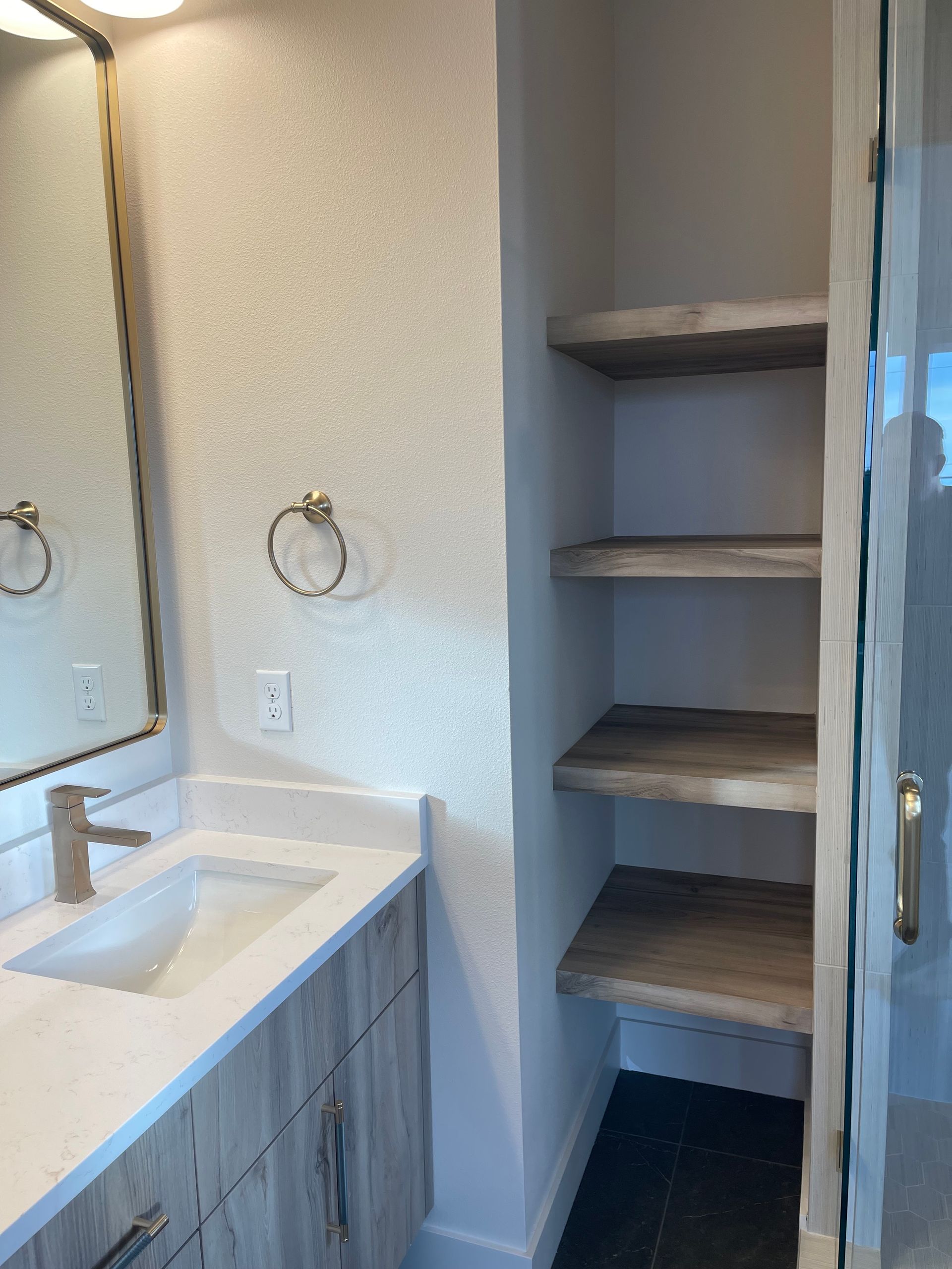 Bathroom with vanity and built-in shelves next to a glass shower door.