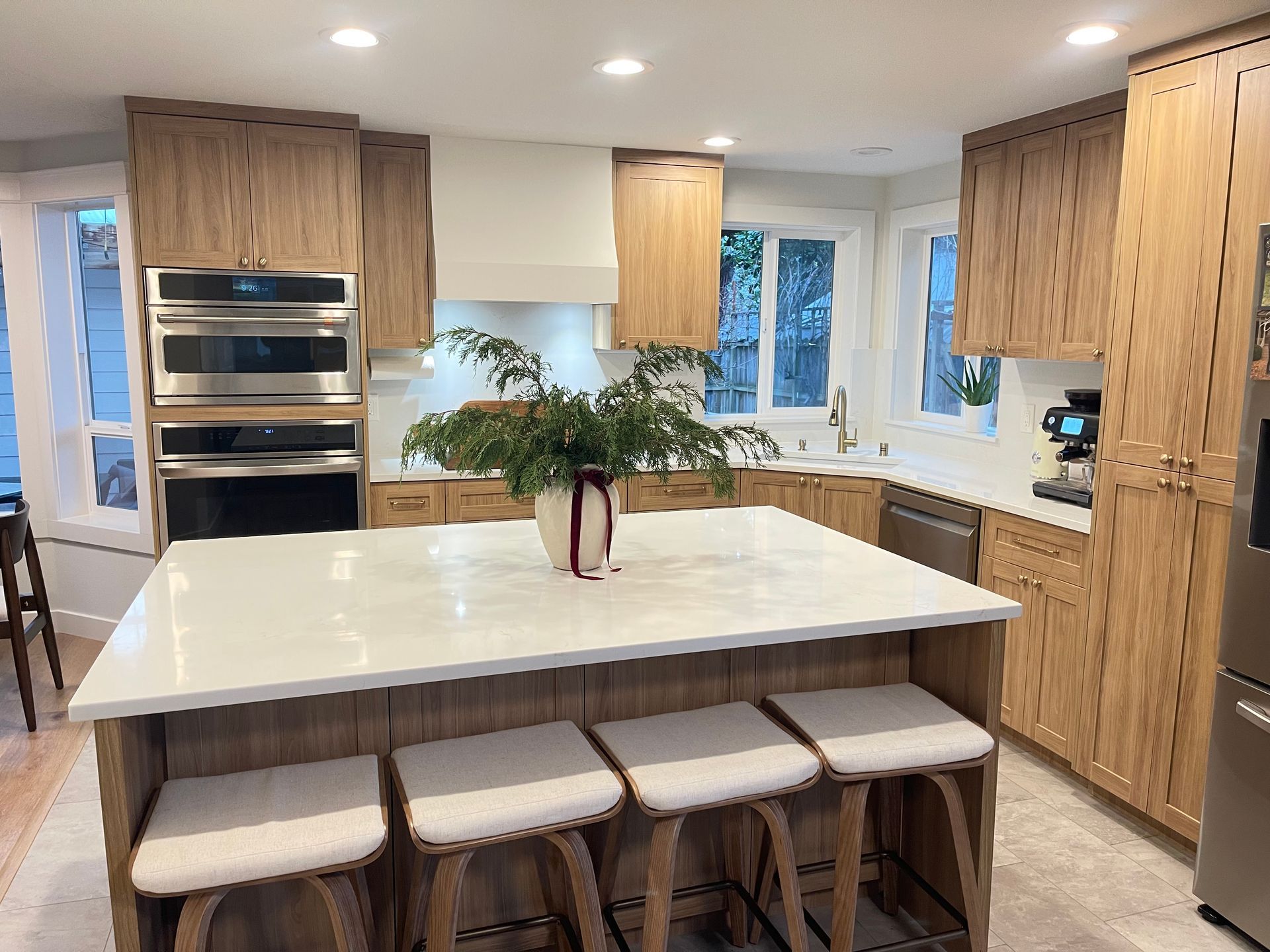 Modern kitchen with light oak cabinets, white countertops, and an island with stools.