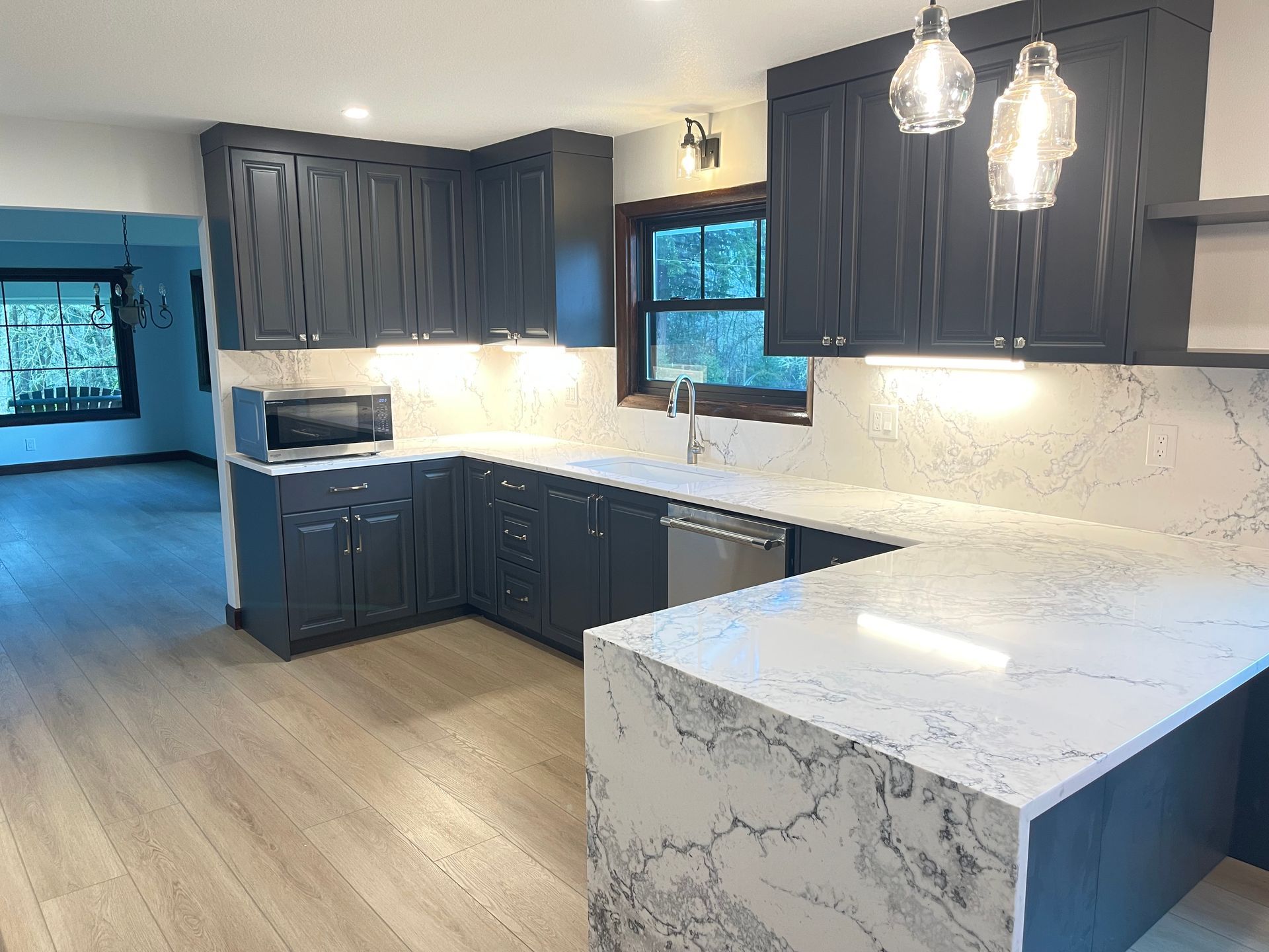 Dark blue kitchen cabinets, white countertops, stainless steel appliances, and wood floors.