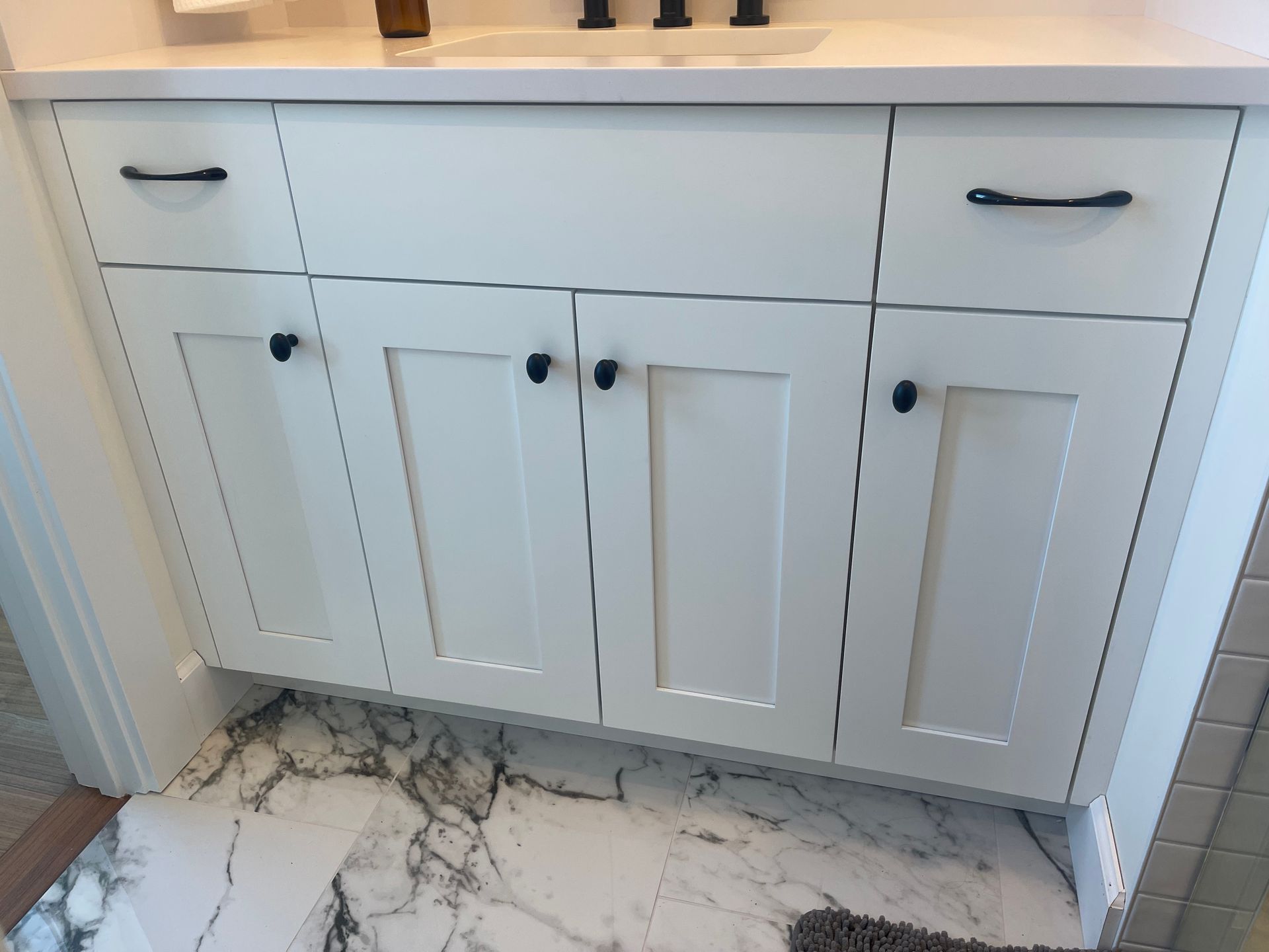 White bathroom vanity with black hardware on marble floor.