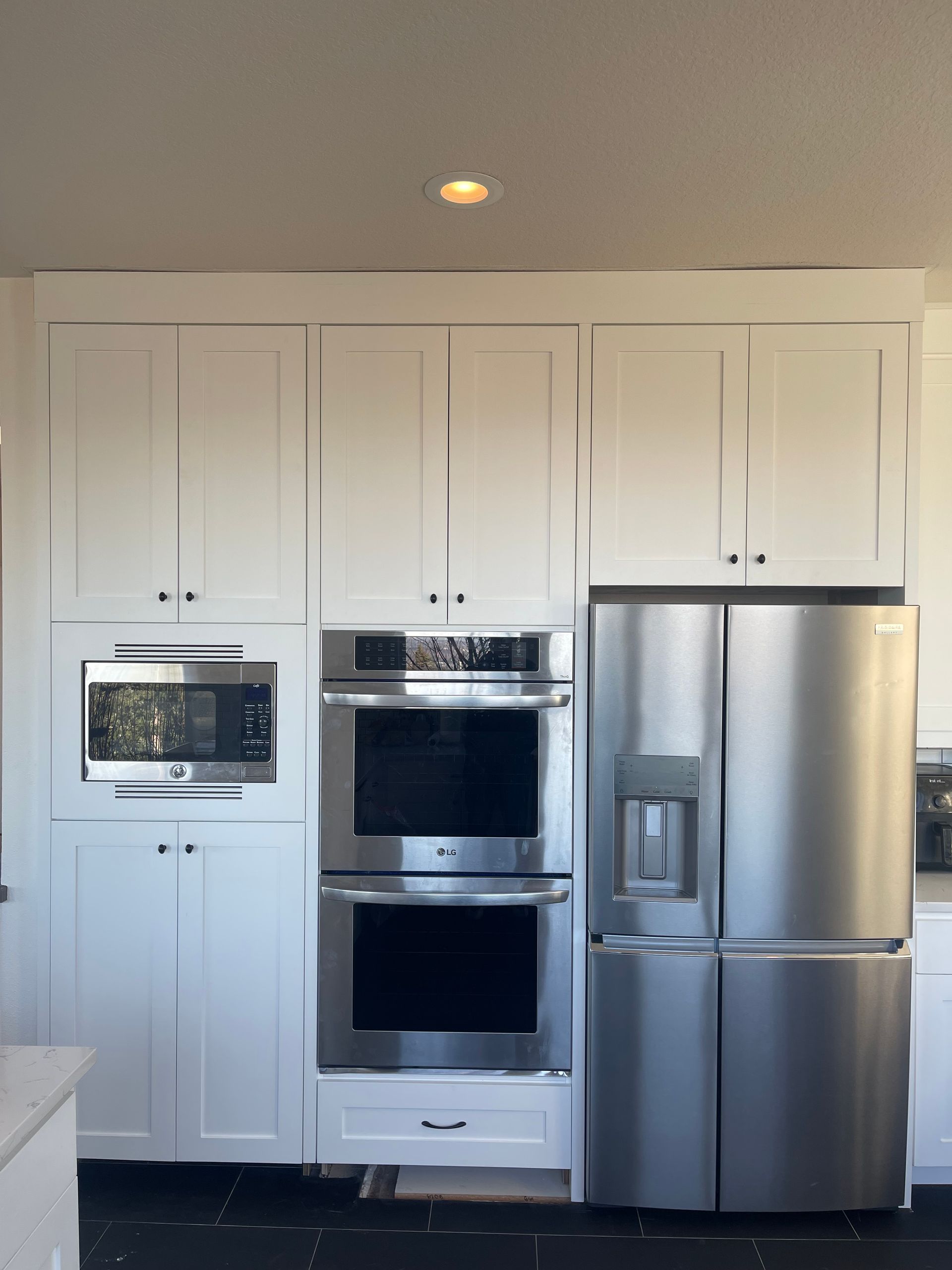 White kitchen cabinets with stainless steel appliances: microwave, double oven, and refrigerator.
