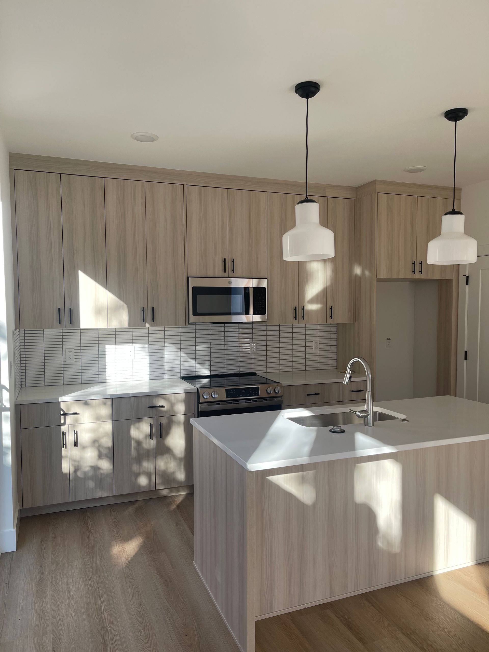 Modern kitchen with light wood cabinets, white countertops, and black hardware.