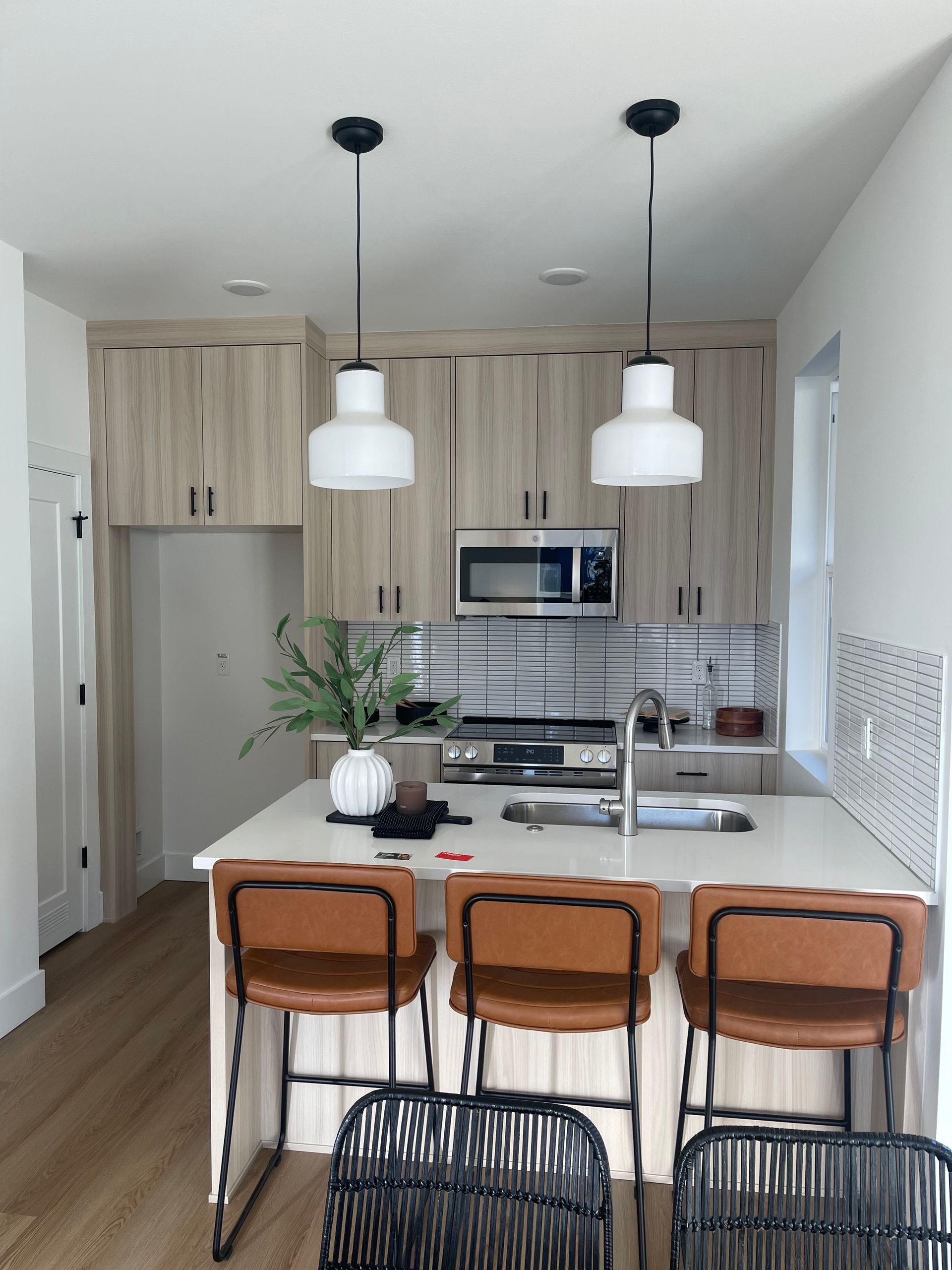 Kitchen with light wood cabinets, white countertops, two pendant lights, and brown leather bar stools.
