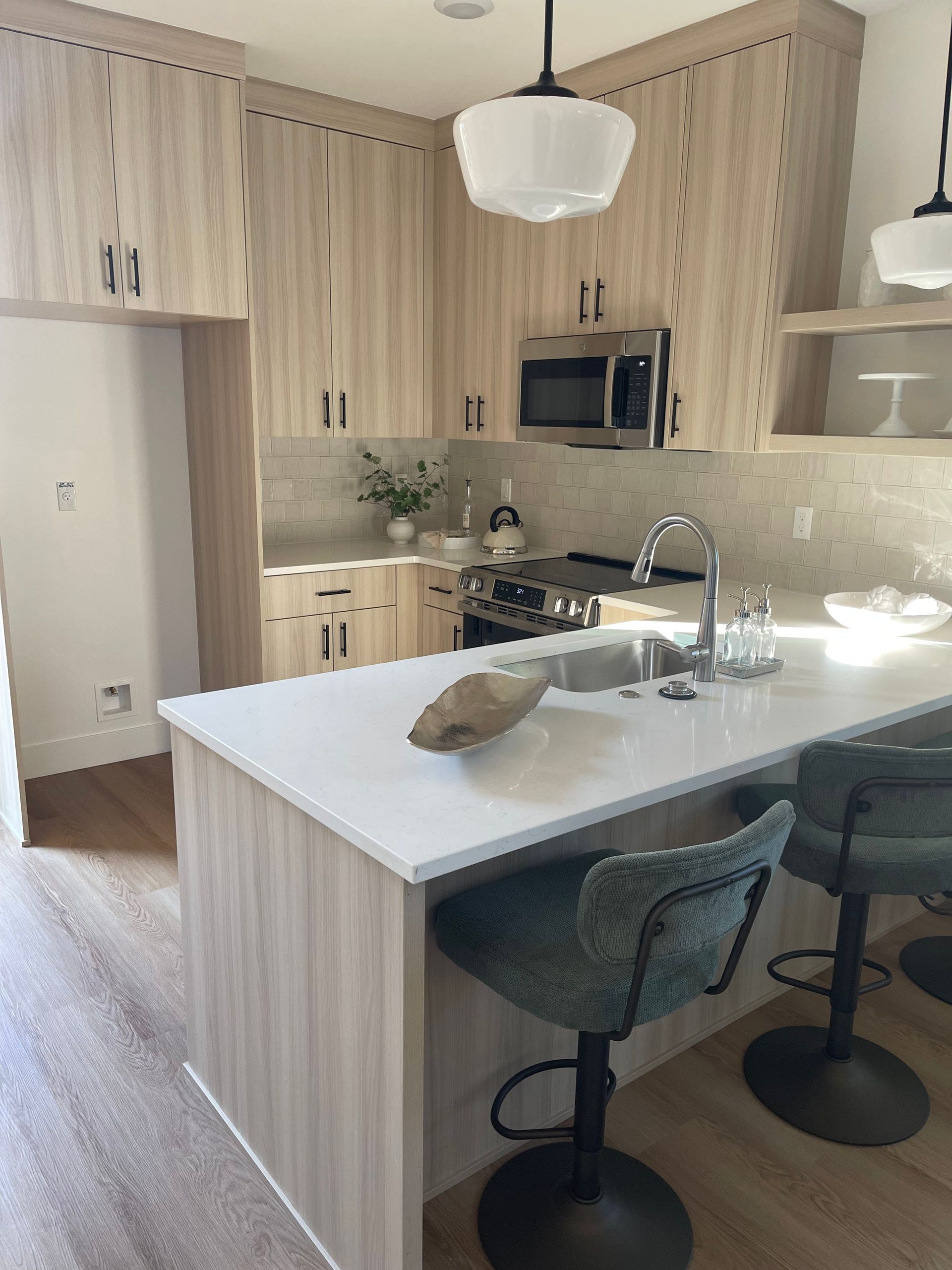 Modern kitchen with light wood cabinets, white countertops, and teal bar stools.