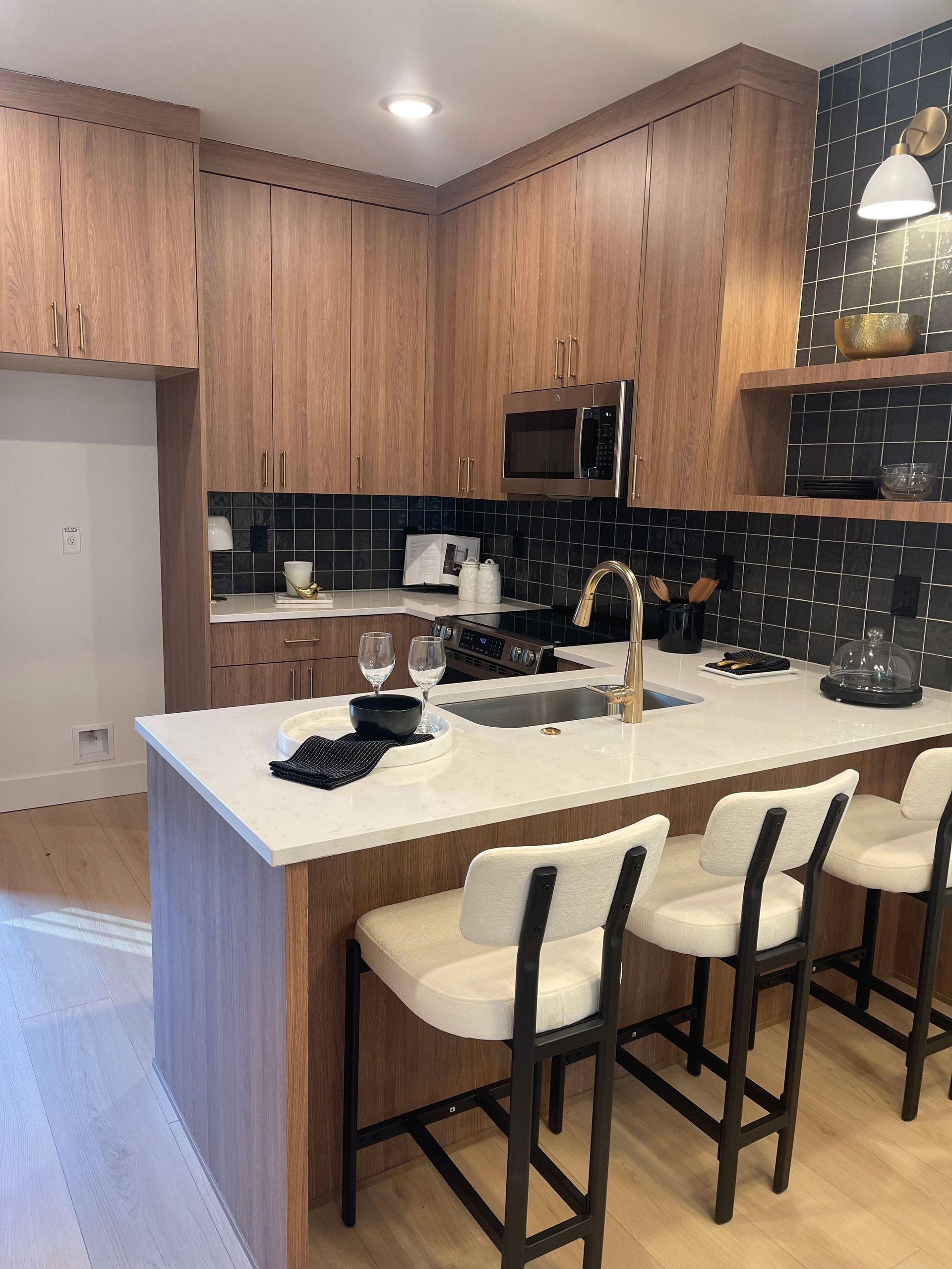 Modern kitchen with wooden cabinets, white countertops, island with bar stools, and black backsplash.