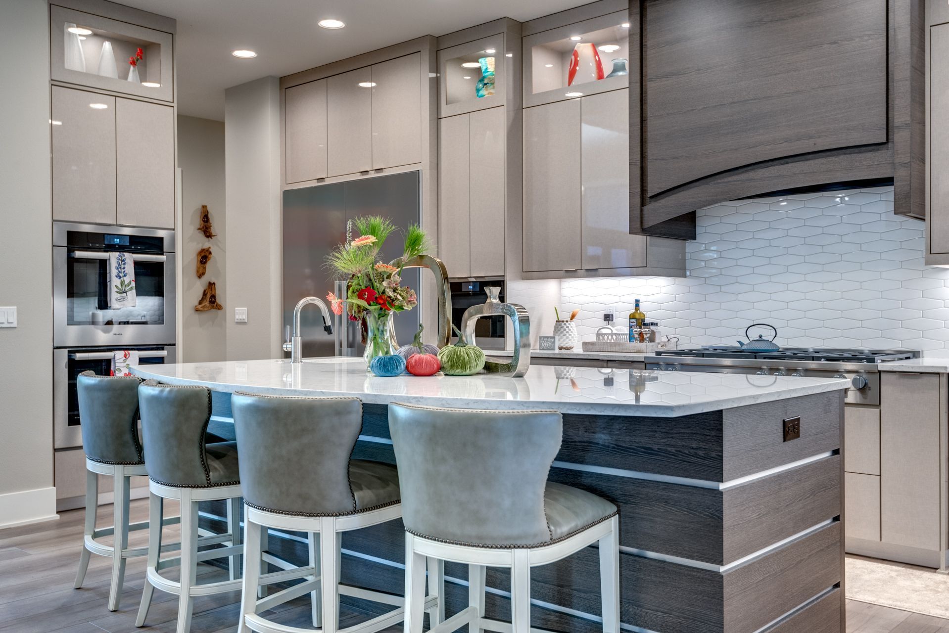 Modern kitchen with island, grey cabinetry, stainless steel appliances, and seating.