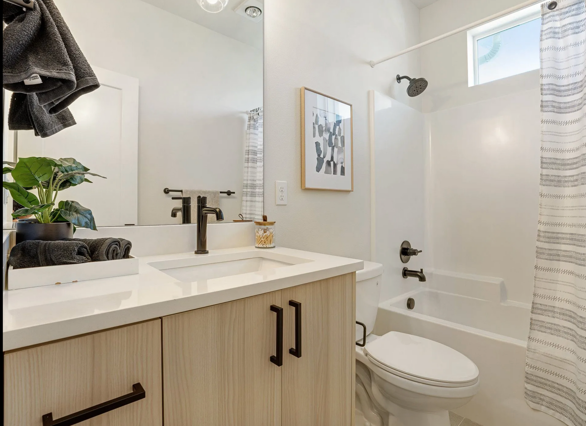 Bathroom with light wood vanity, white sink, black fixtures, white toilet, and tub.