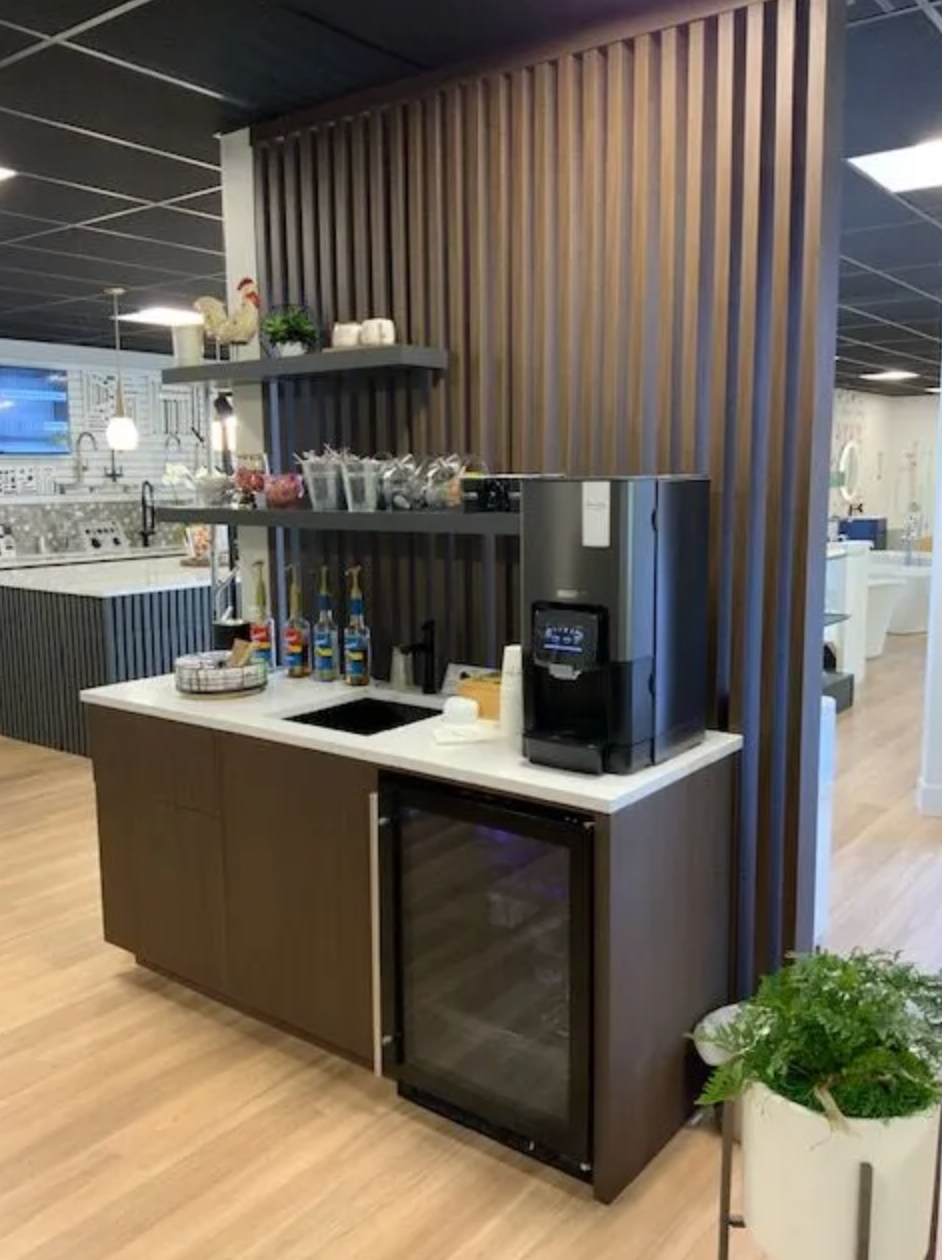 Coffee station with brown cabinets, refrigerator, water dispenser, and shelves. Light wood floor.