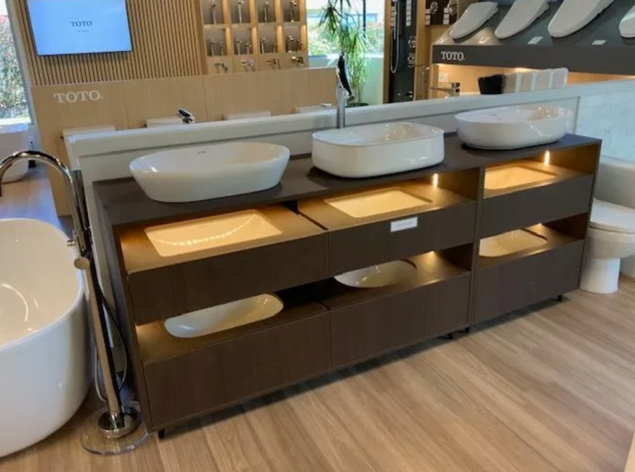 Bathroom fixture display with dark brown cabinet, showcasing sinks, with wooden floors.