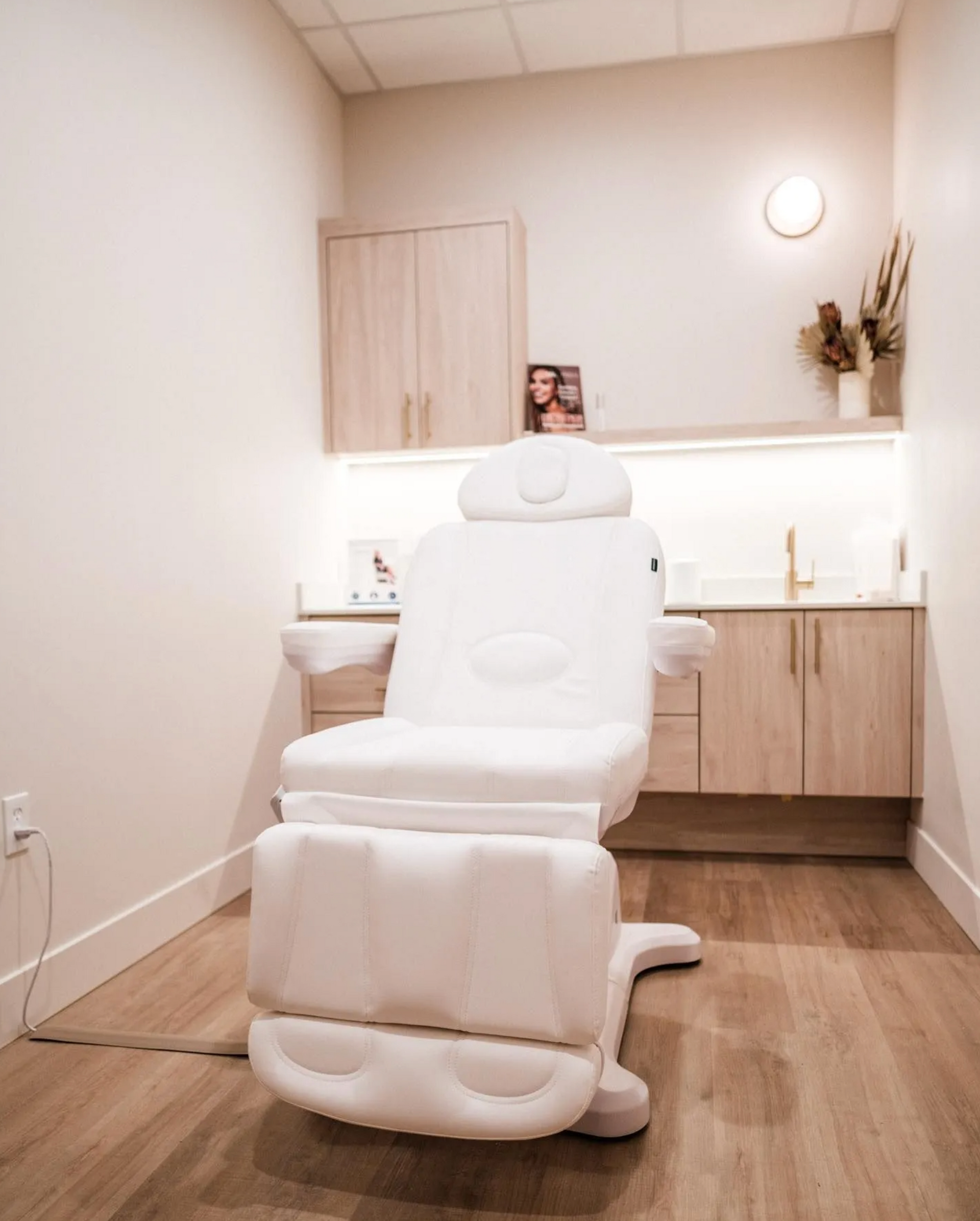 White medical chair in a bright treatment room. Wooden cabinets and flooring.