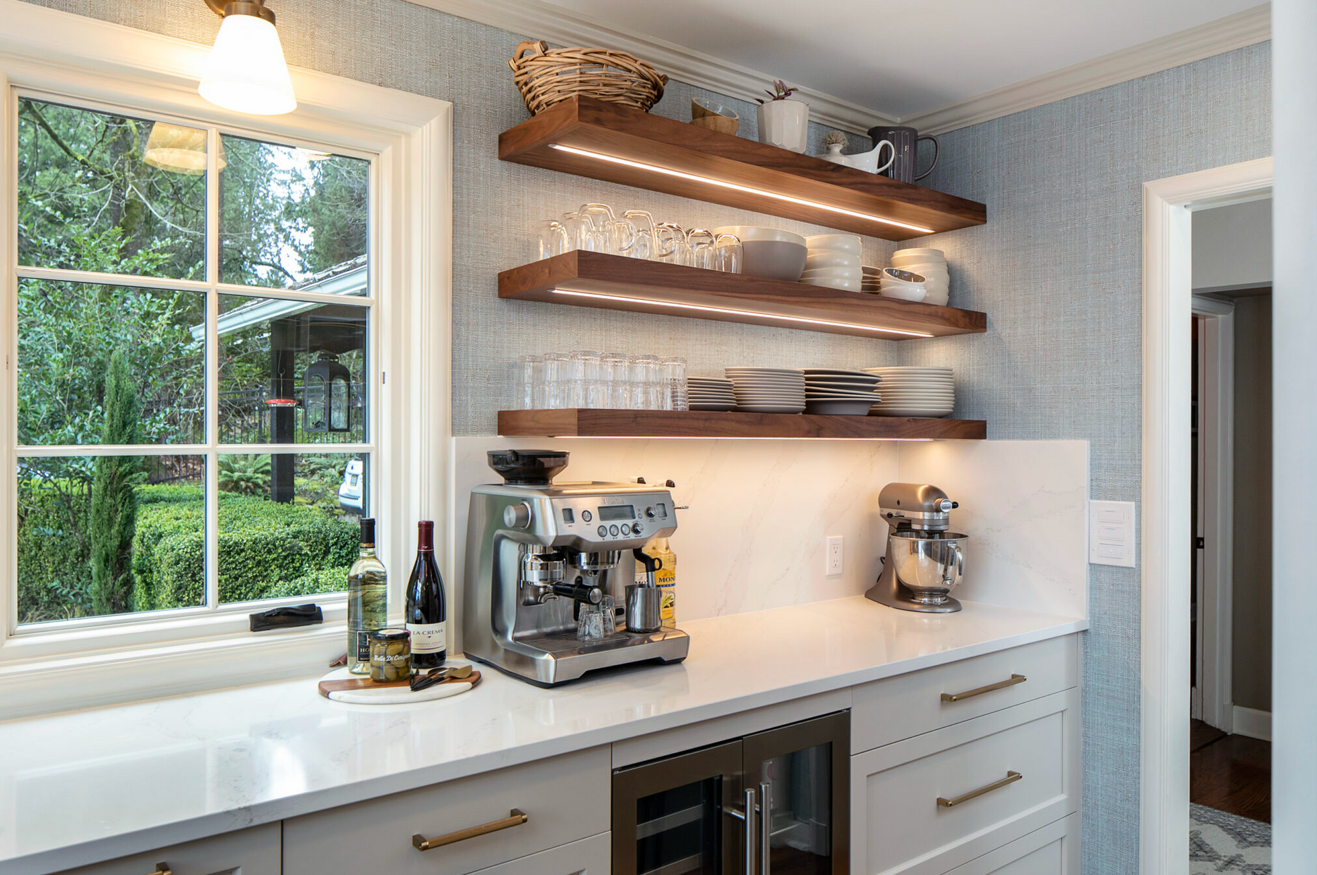 Kitchen with espresso machine, open shelves, window, and light blue textured wallpaper.