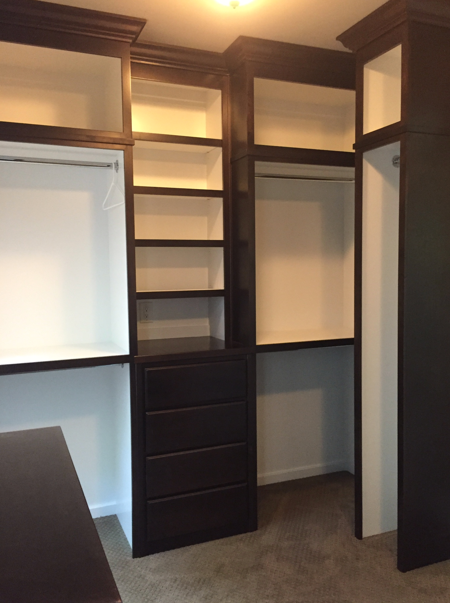 Walk-in closet with dark stained cabinetry. White shelving and walls, drawers, and hanging rods.