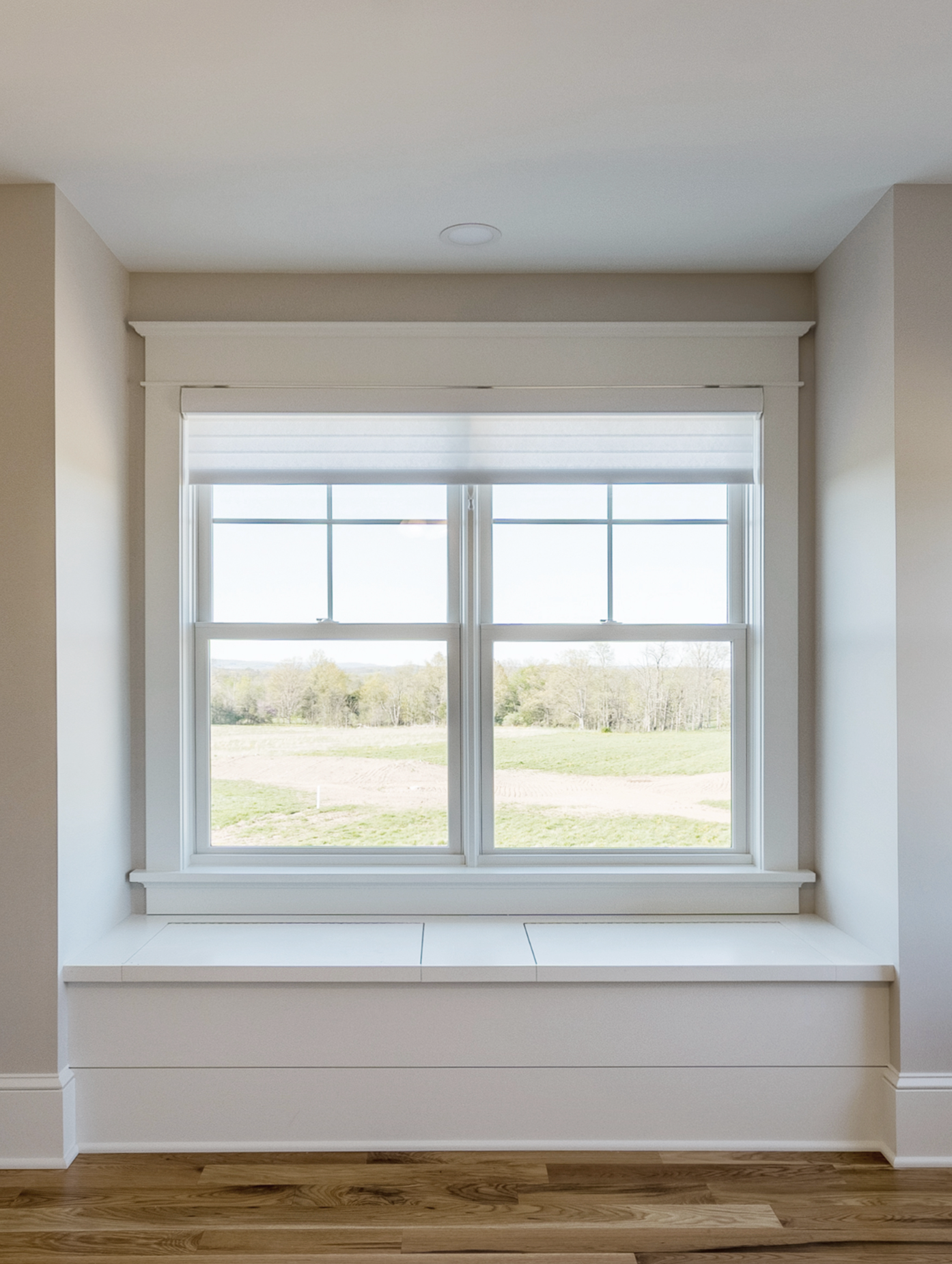 Window with white trim and a built-in bench, offering a view of a grassy field.