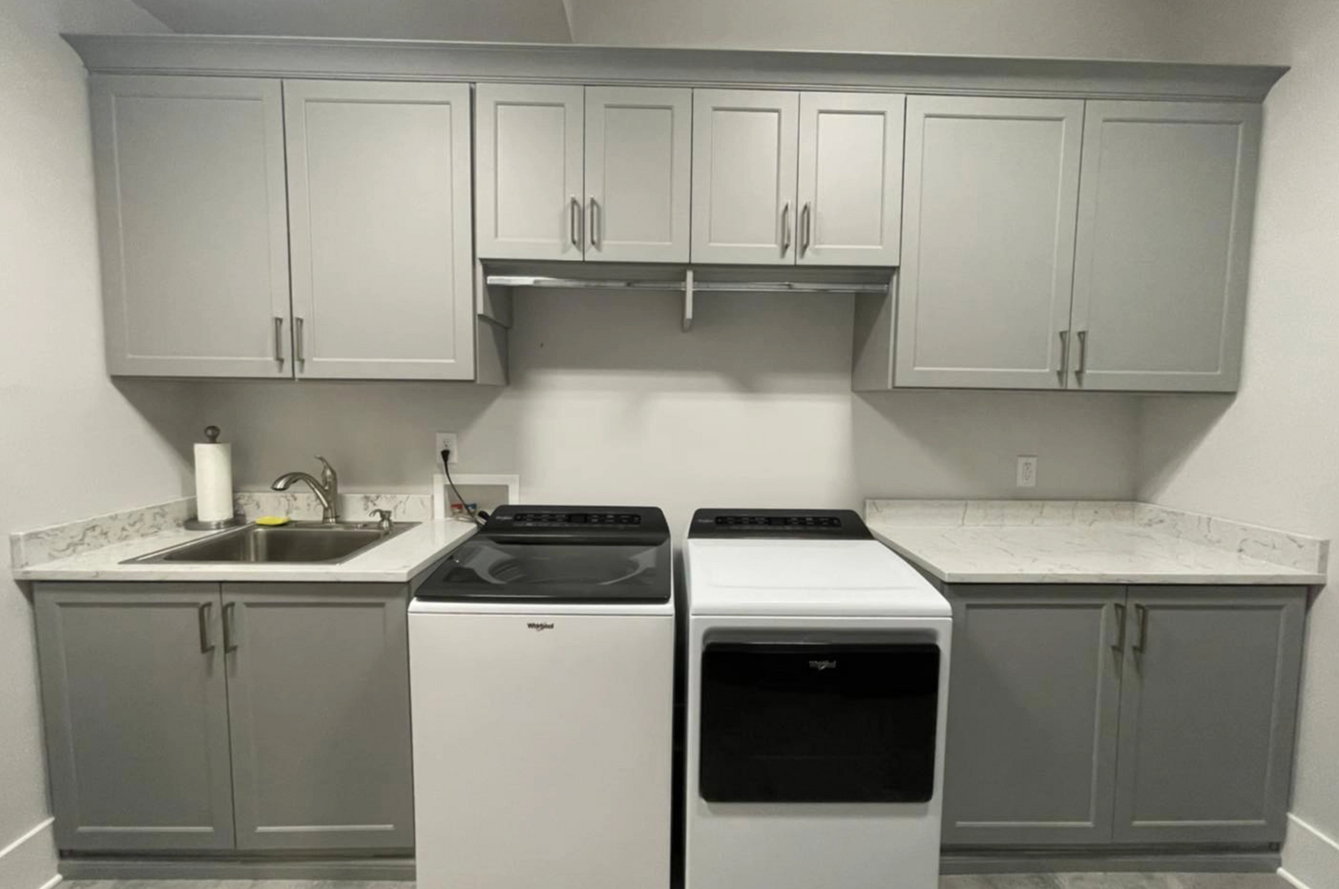 Laundry room with grey cabinets, white appliances, and a sink.