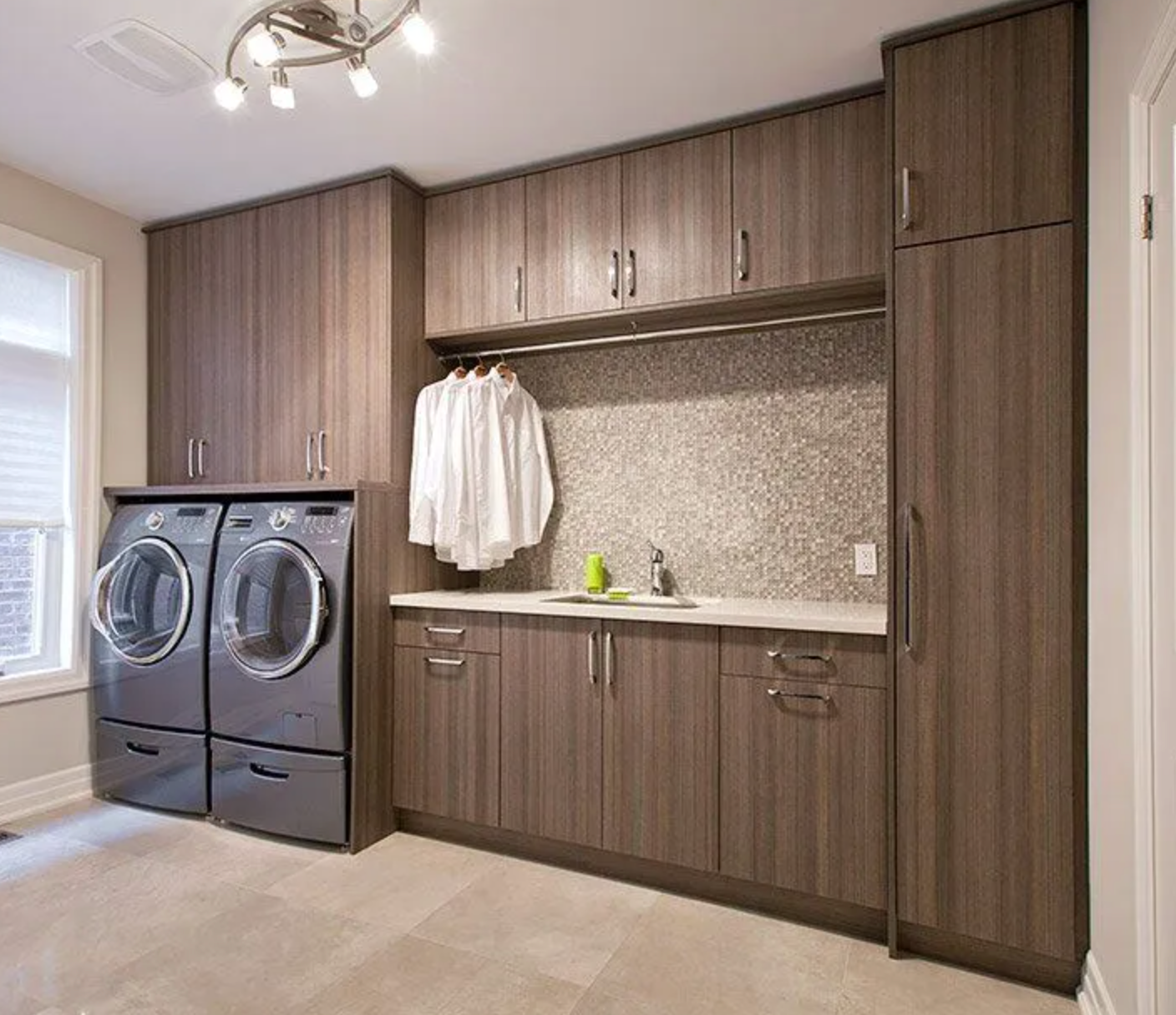 Modern laundry room with dark wood cabinets, washer/dryer, and hanging rod.