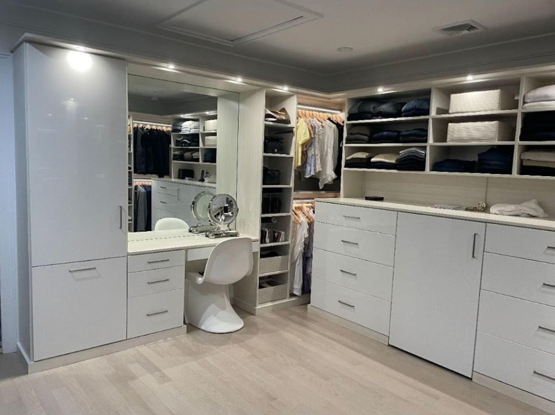 White, modern walk-in closet with shelves, drawers, hanging rods, and a vanity.