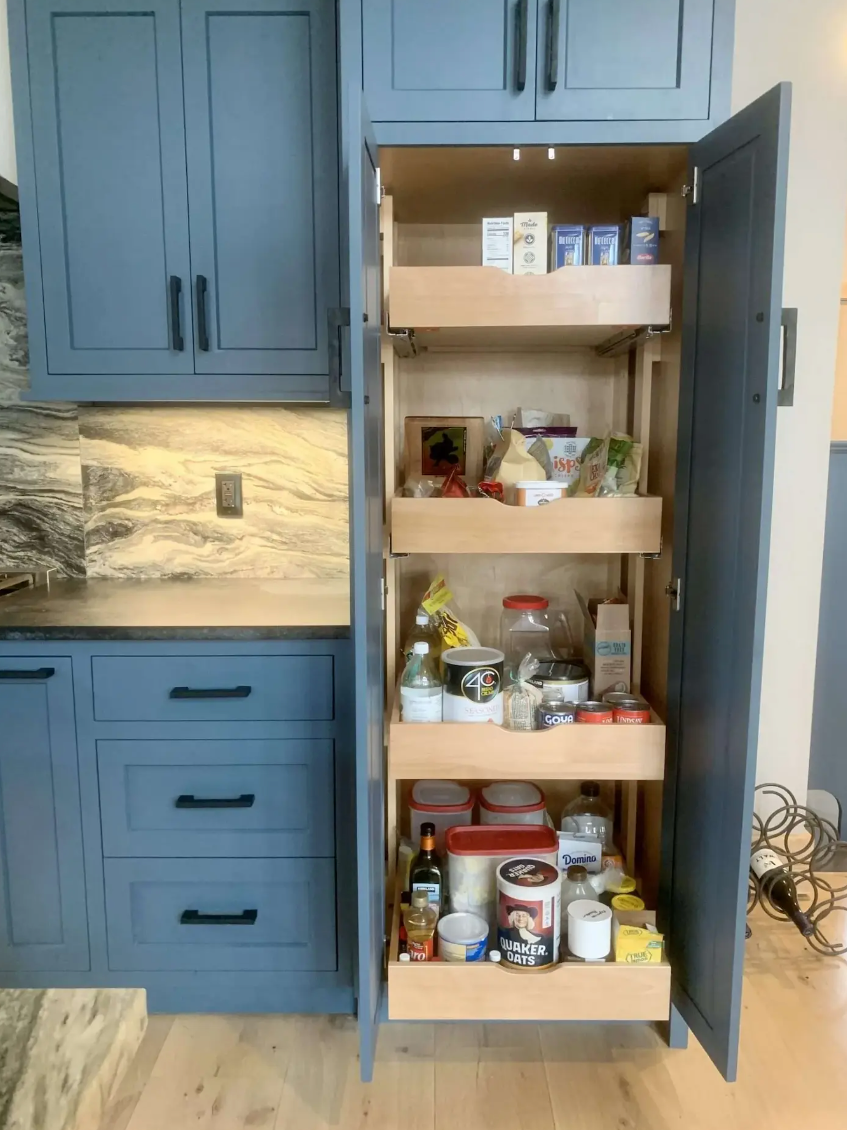 Blue kitchen pantry cabinet open, revealing shelves with groceries.