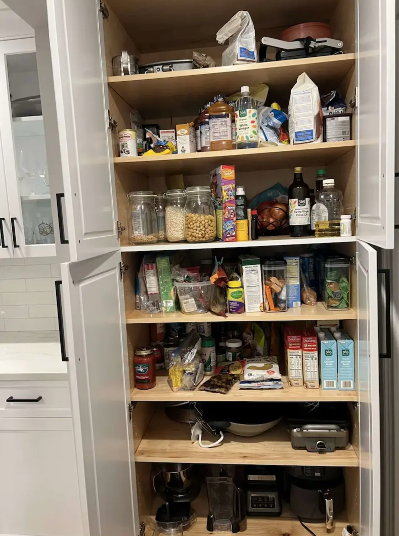 A tall, white kitchen pantry filled with various food items and small appliances.