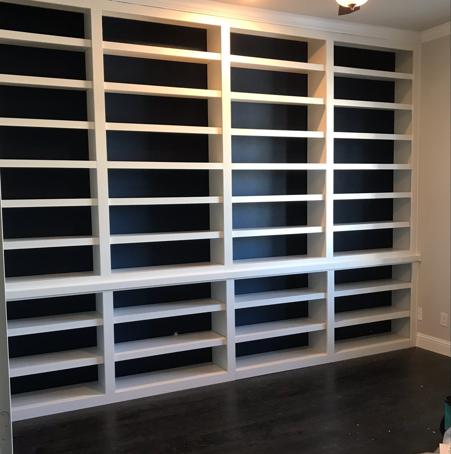 Empty white built-in shelving wall in a room with dark floor and dark backing.
