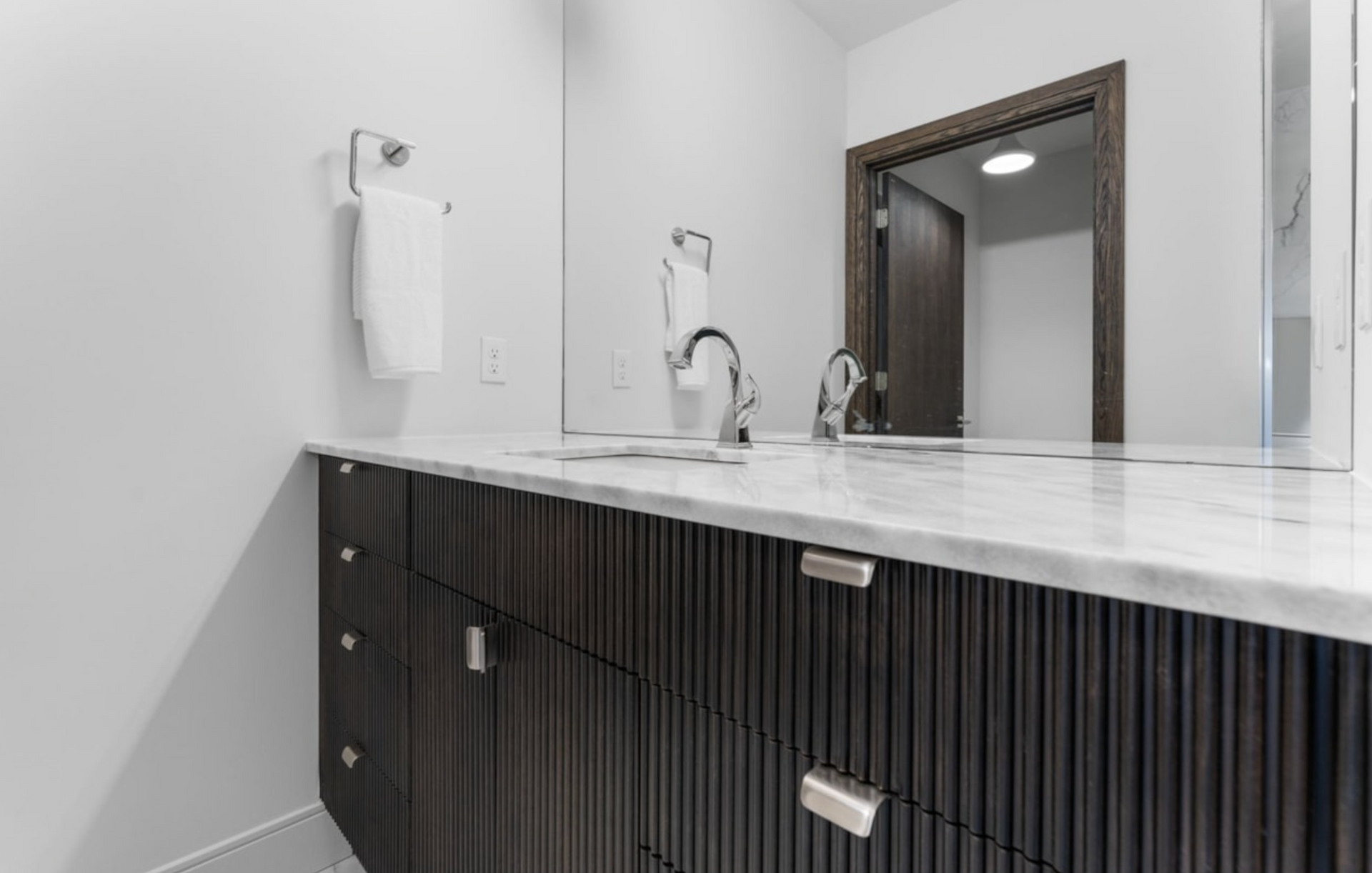 Modern bathroom with dark wood vanity, white marble countertop, and chrome fixtures.