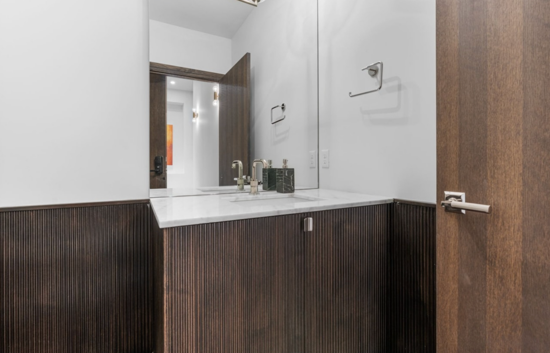 A small modern bathroom with dark wood paneling, white countertop, and large mirror.