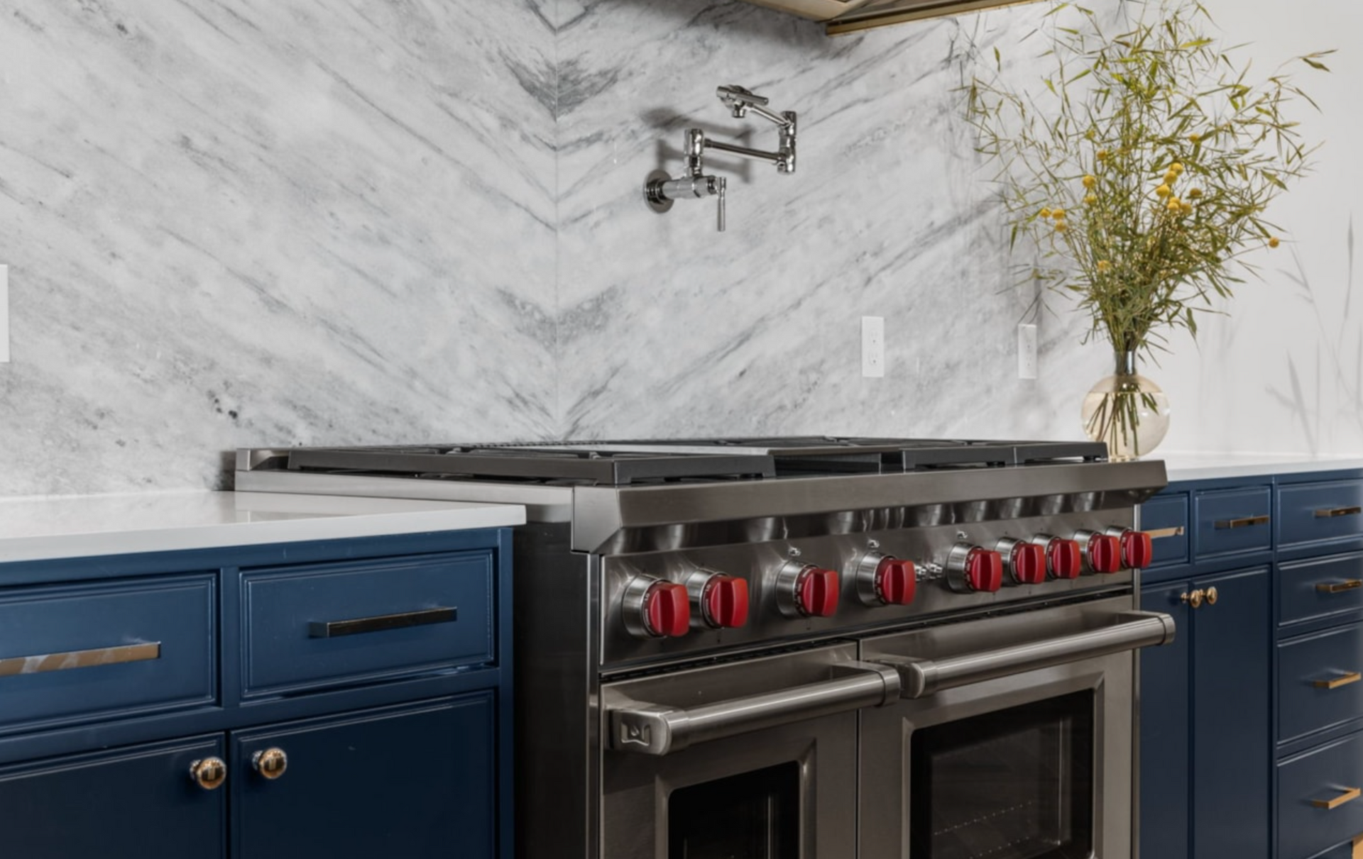 Kitchen with a stainless steel stove, red knobs, and navy blue cabinets with marble backsplash.