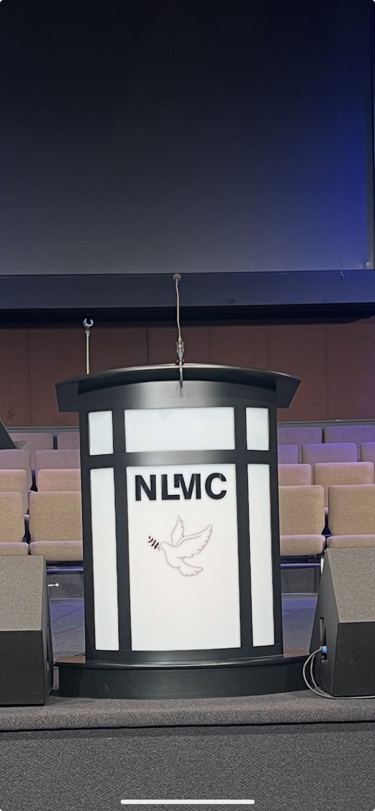 Podium with NLMC logo on a stage, lit against a dark blue backdrop.