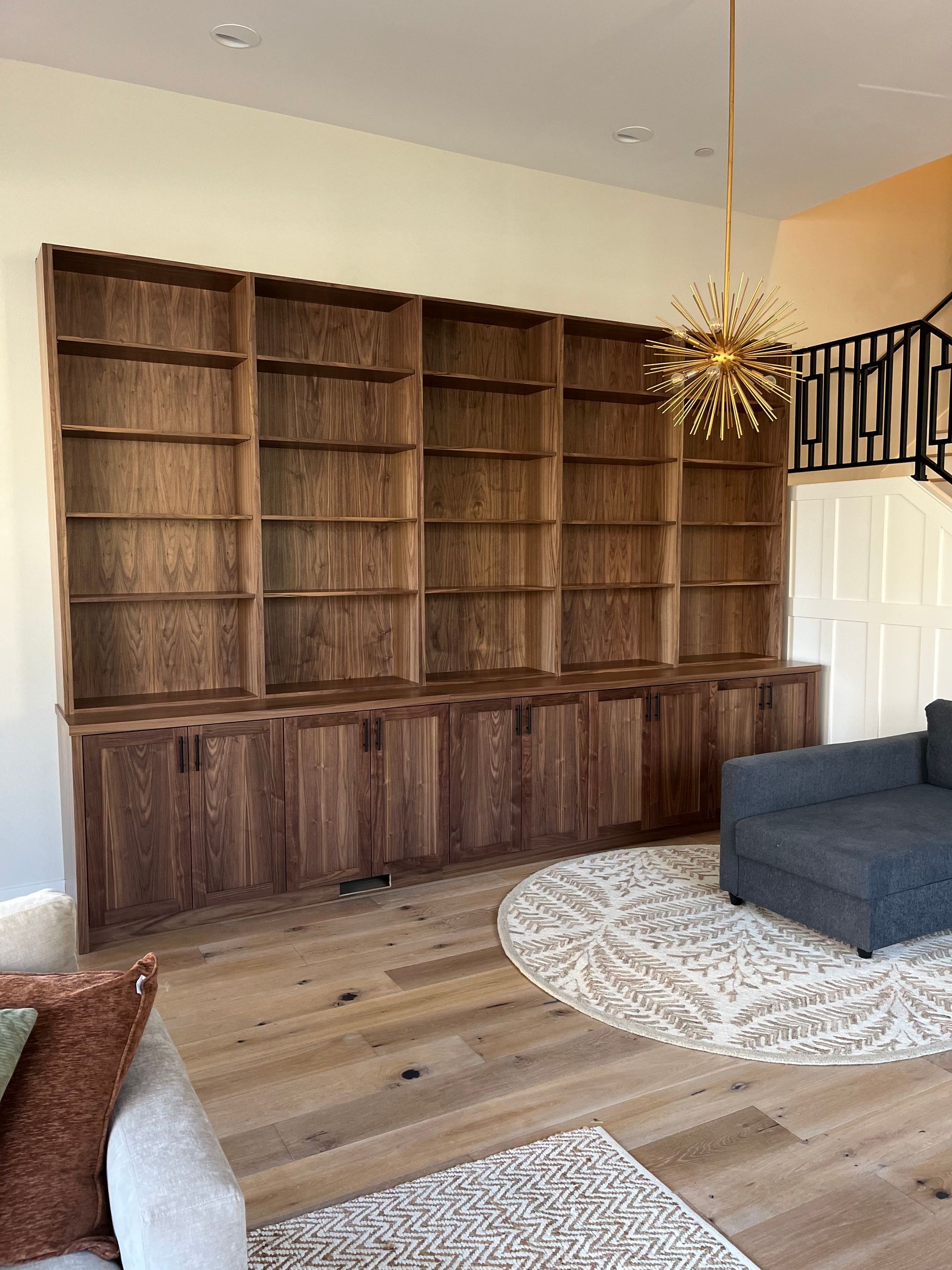 Living room with built-in wooden bookcases, gray sofa, round rug, and modern pendant light