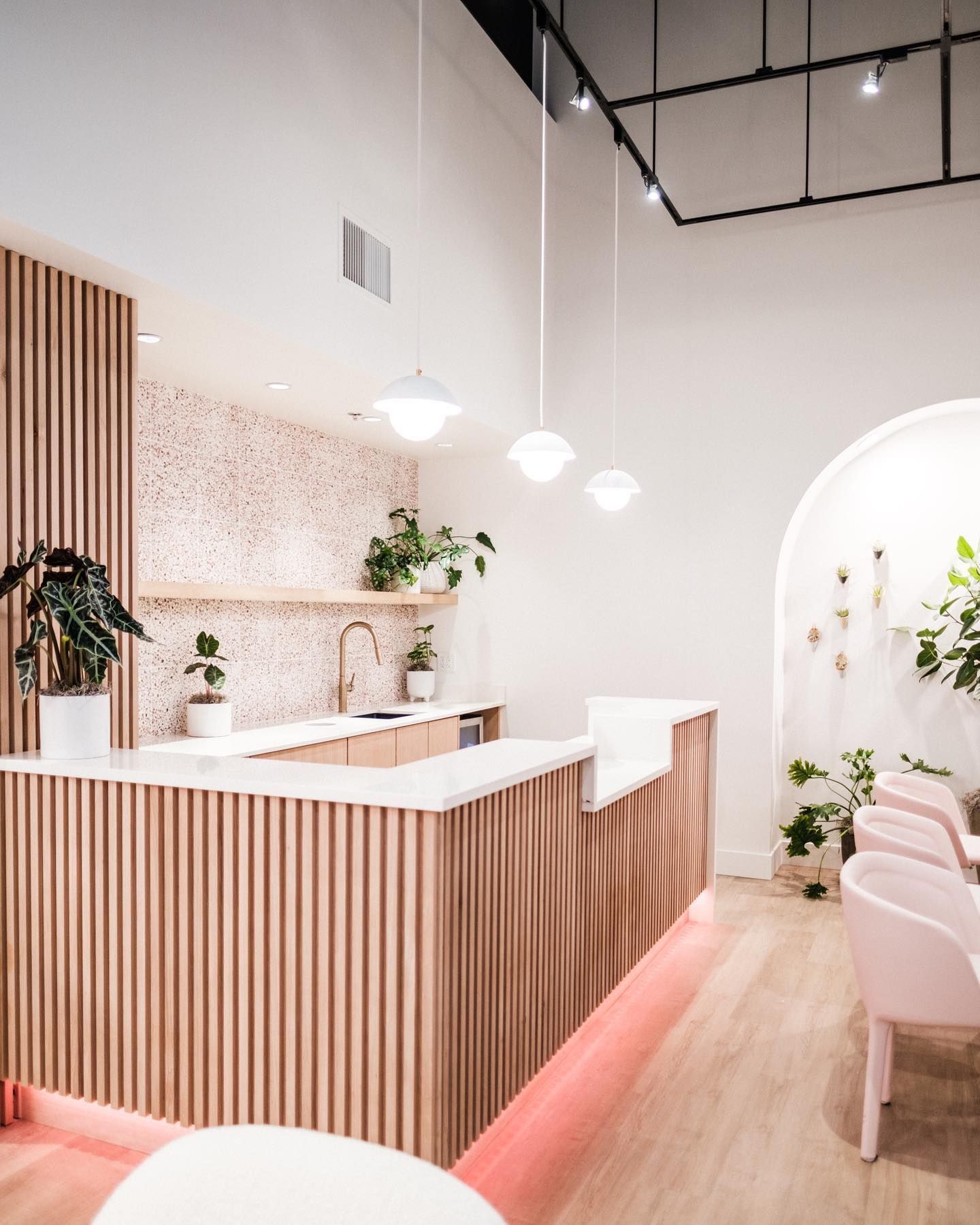 A modern, pink-toned cafe interior with a counter, plants, and globe pendant lights.