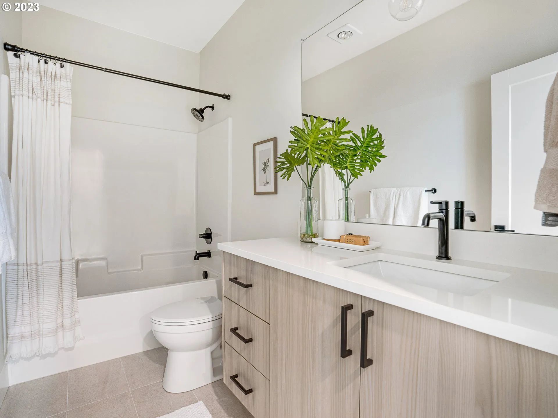 Modern bathroom with white walls, light wood vanity, and black fixtures.