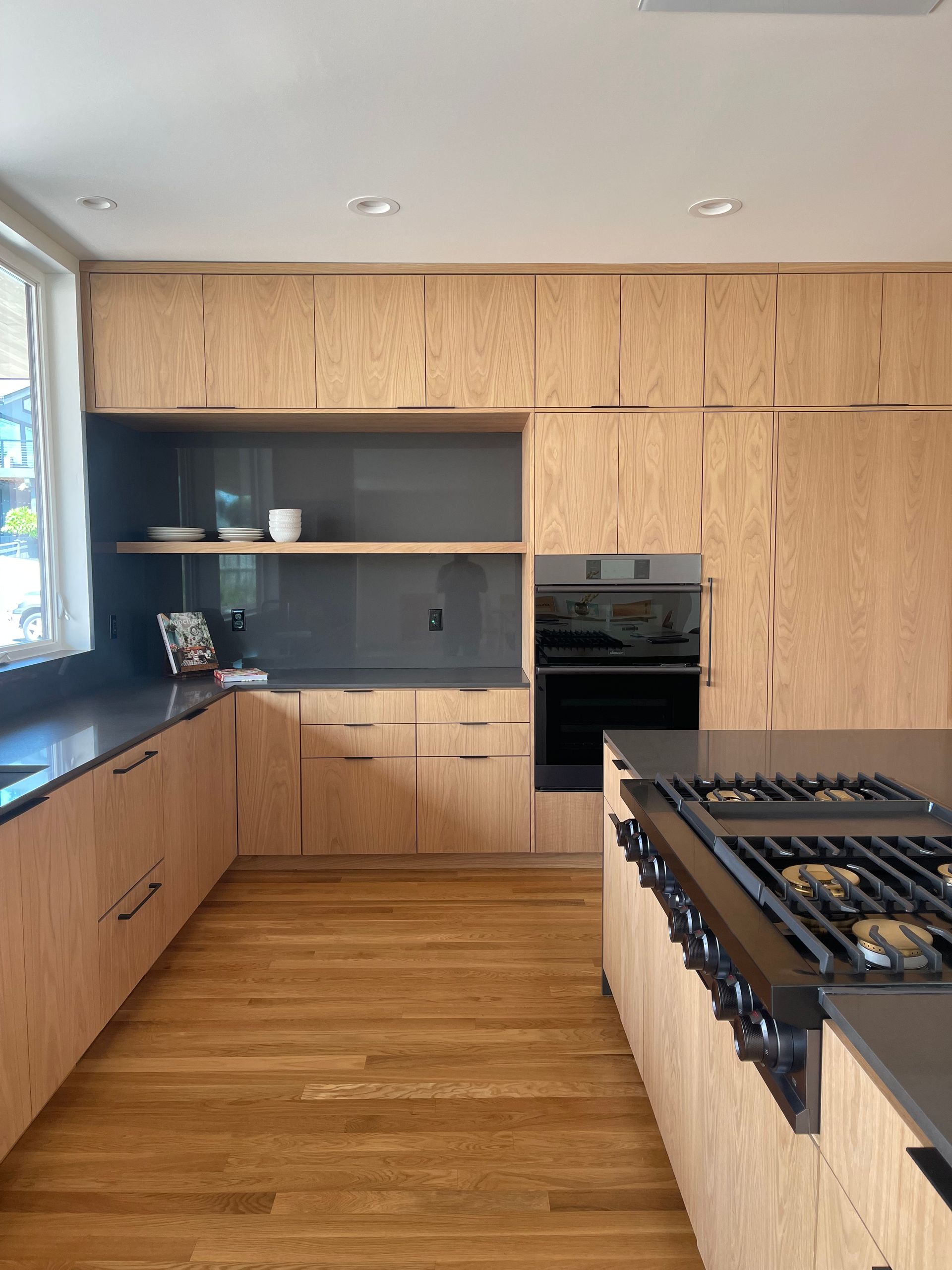 Modern kitchen with light wood cabinets, dark countertops, and stainless steel gas range.