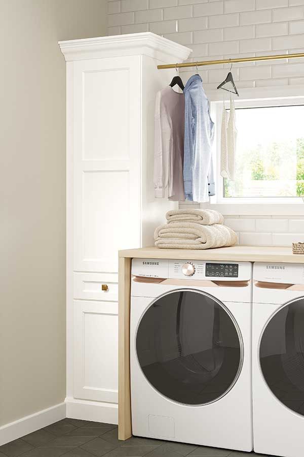 Laundry room with a washing machine, dryer, and cabinet. Clothes hang on a rod near a window.