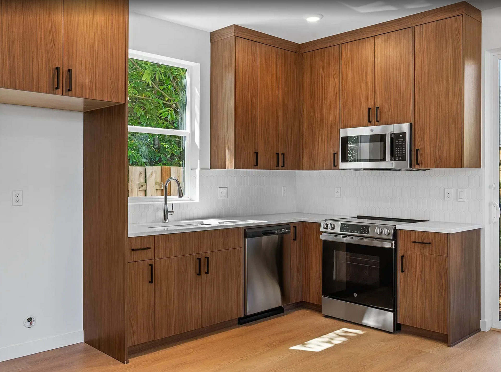 Kitchen with brown cabinets, stainless steel appliances, white backsplash, and a window.