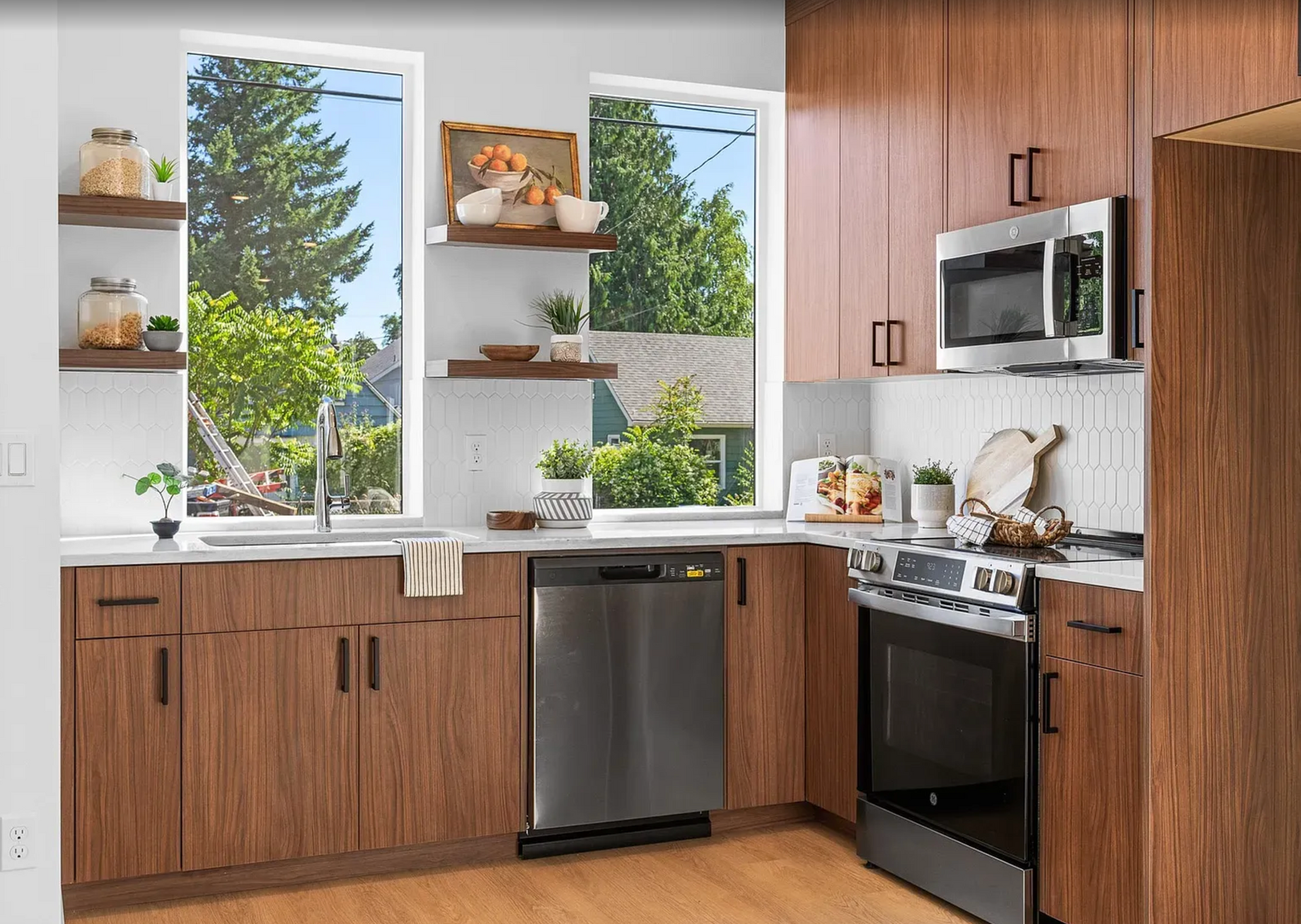 Modern kitchen with walnut cabinets, stainless steel appliances, and large windows overlooking trees.