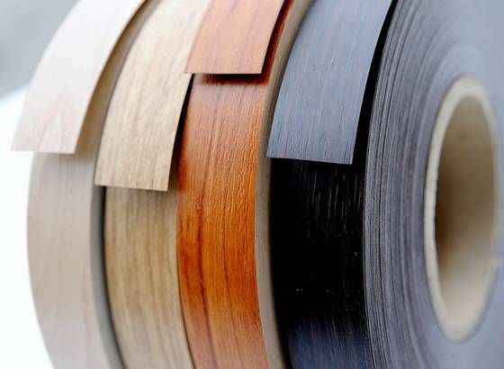 Spools of wood veneer edging in beige, orange, black, and gray on rolls