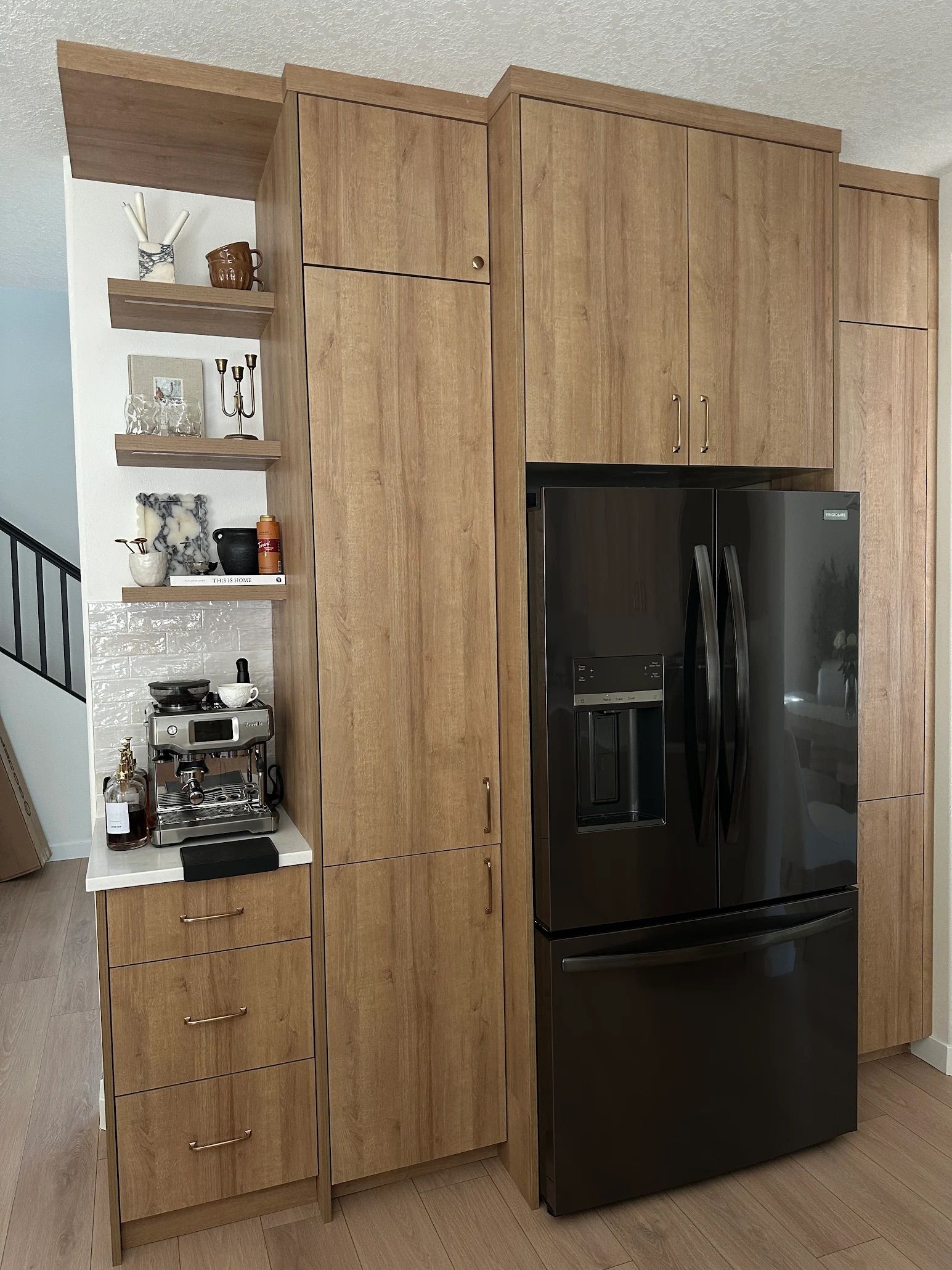 Built-in wooden cabinets with a black refrigerator. Open shelves to the left, drawers below, all in a kitchen setting.