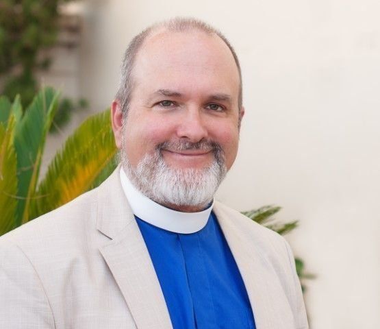 A man with a beard is wearing a white collar and a blue robe.