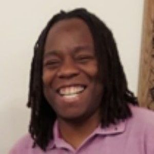 A man with dreadlocks is smiling and wearing a purple shirt.