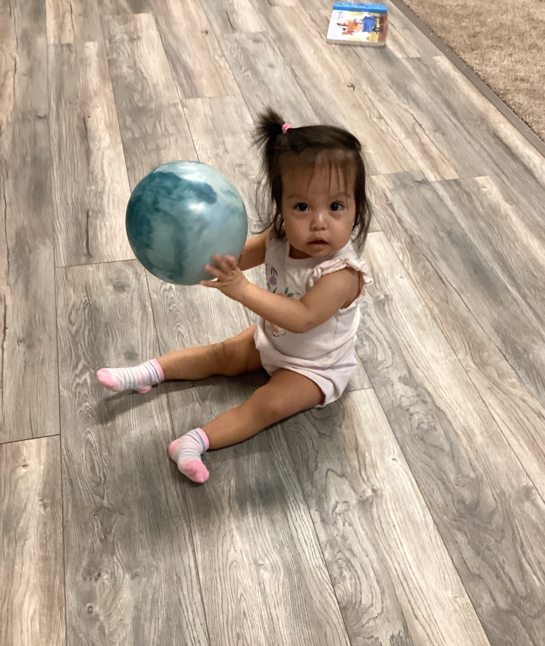 A little girl is sitting on the floor holding a ball.