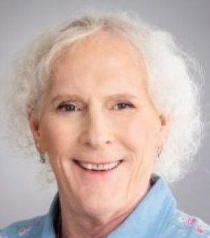 A person with white hair is smiling and wearing a blue shirt.