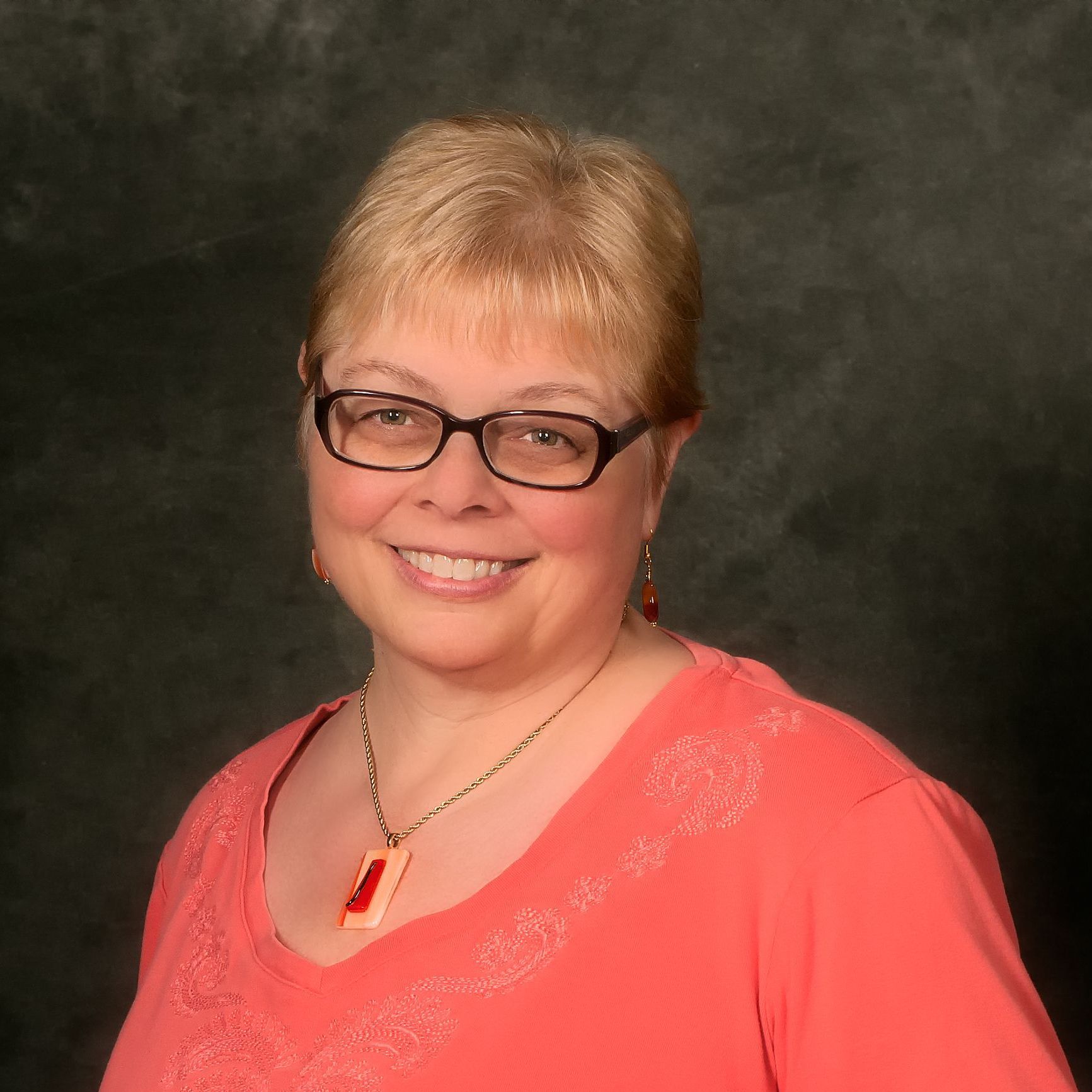 A woman wearing glasses and a red shirt smiles for the camera