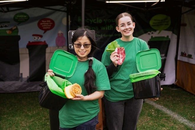 Community members gather at a FOGO event hosted by Parramatta Council, learning about food waste reduction and composting. A presenter demonstrates how to separate food scraps for organic recycling, with bins and educational materials displayed.