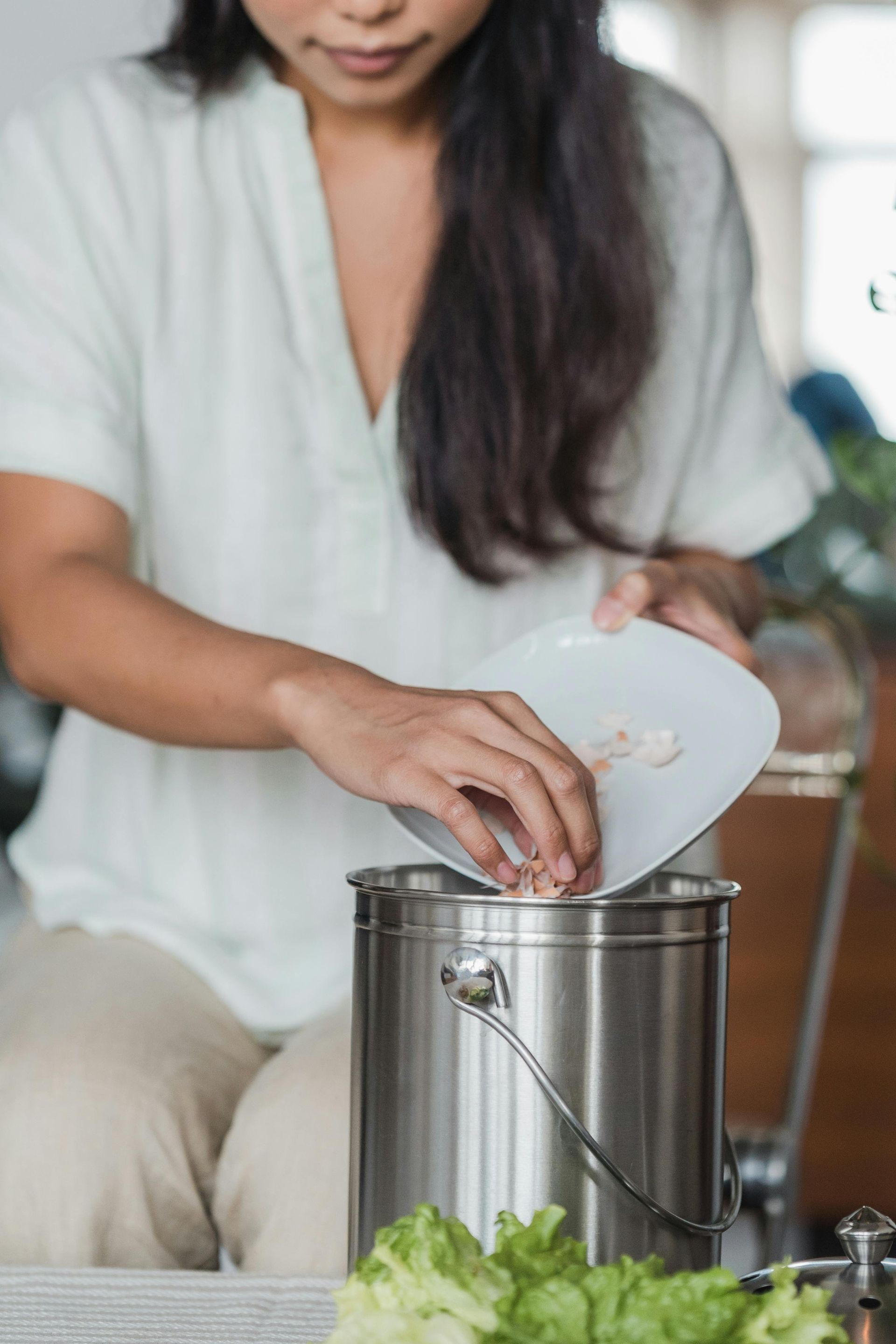 Hands placing vegetable scraps into a compost bin, demonstrating a simple and effective way to reduce food waste.