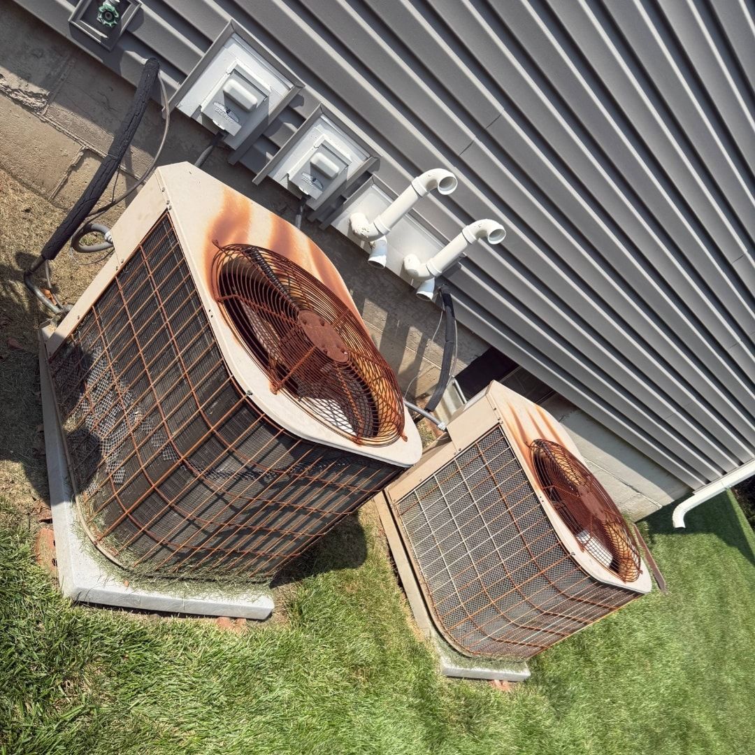 Two rusty air conditioning units sitting on concrete pads next to a building.